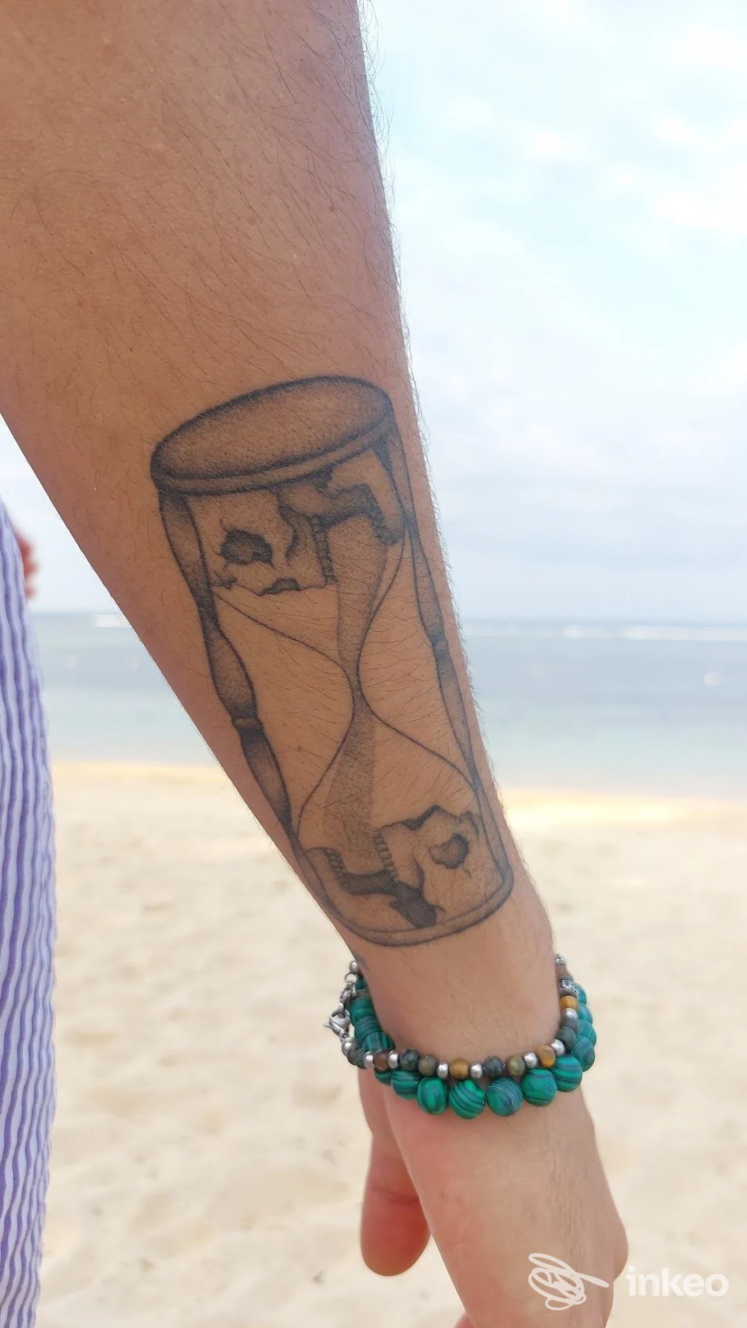 Tatuaggio a clessidra in nero sull'avambraccio, foto scattata in spiaggia. Furioza Tattoo Studio, Terni.