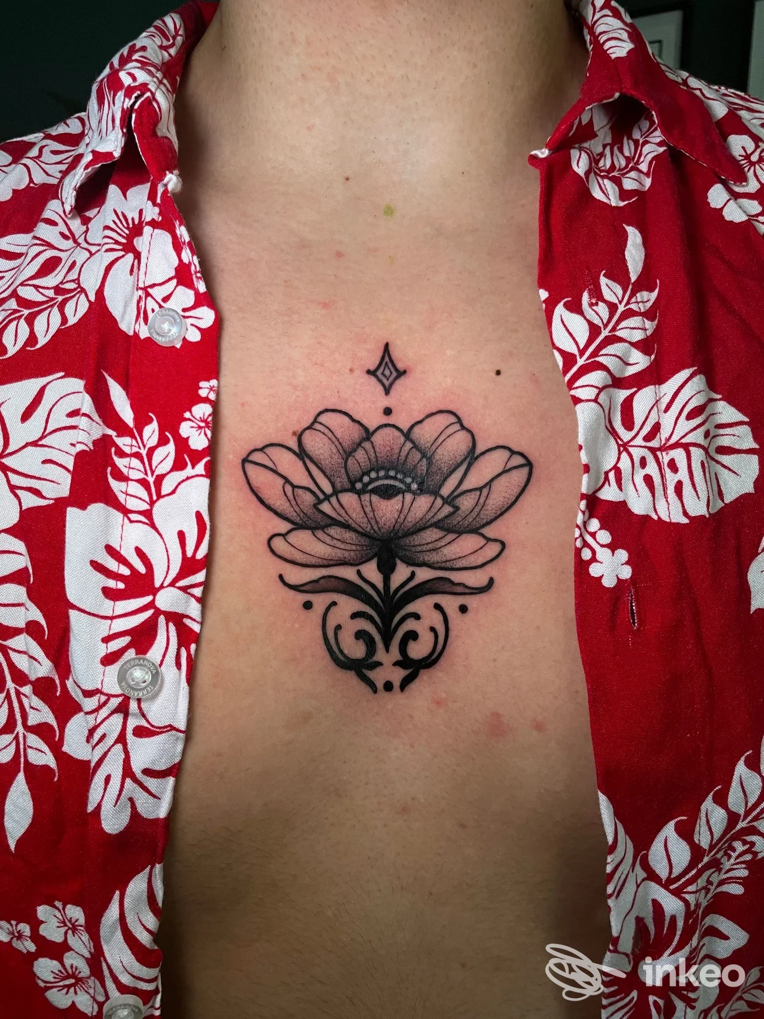 Tatuaggio nero a forma di fiore stilizzato sullo sterno, fotografia in primo piano. Libe tattoo studio, Perugia.