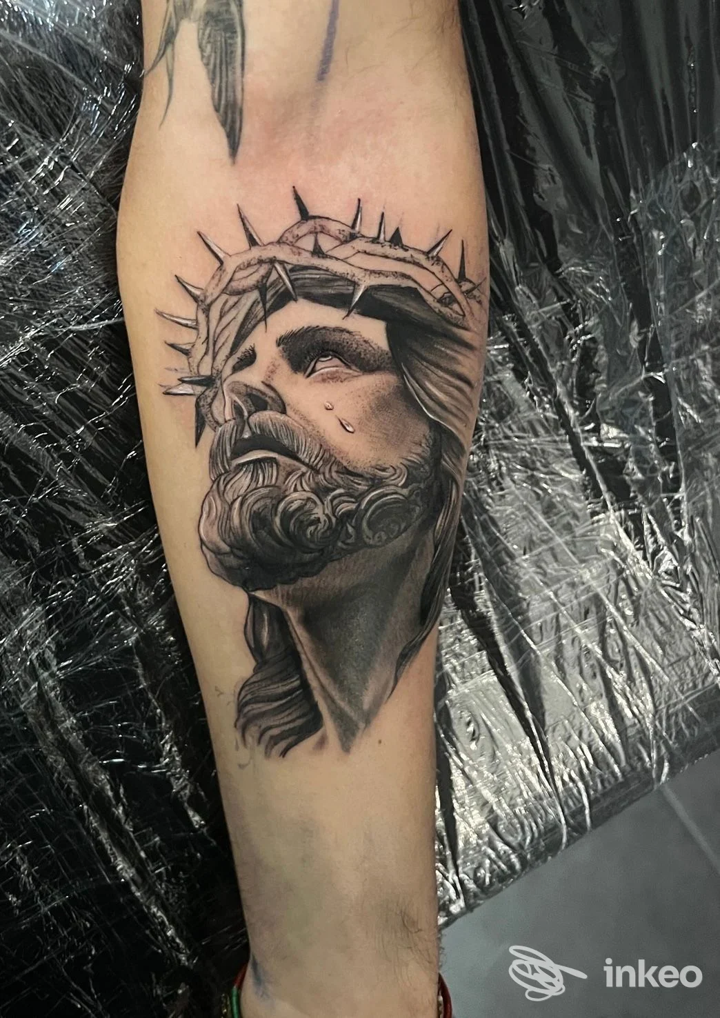 Tatuaggio realistico in bianco e nero del volto di Cristo con corona di spine sull'avambraccio, foto fornita da Ninja Tattoo, Deruta.