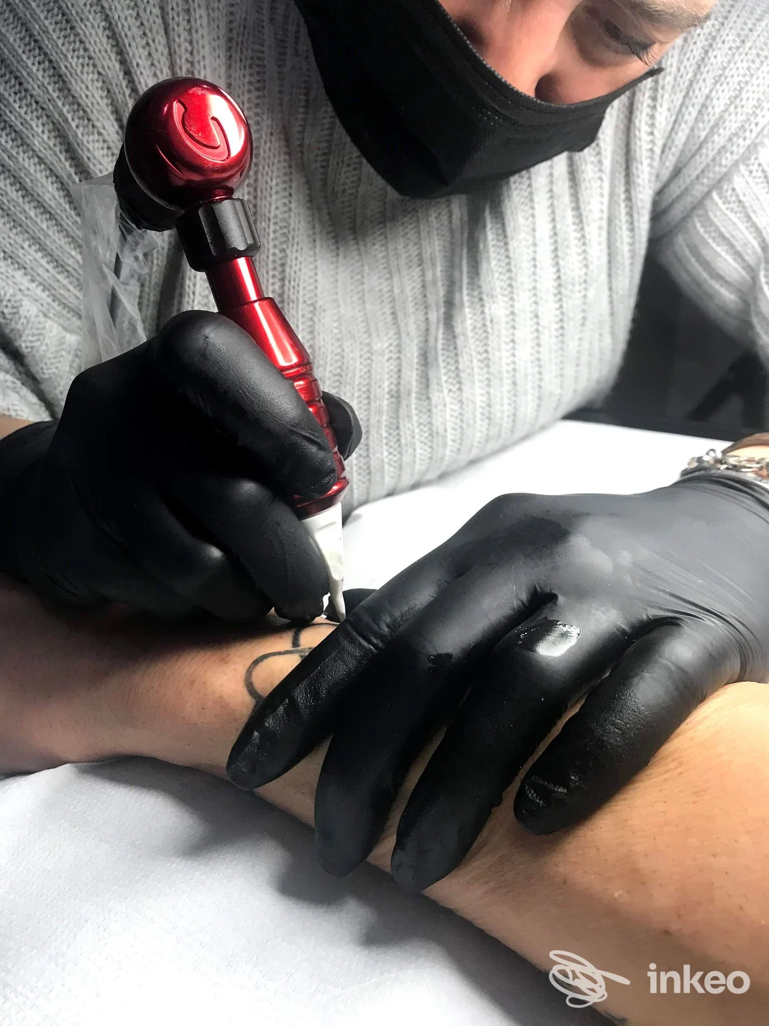 Tatuatore che applica un tatuaggio al polso di un cliente nello studio Sara Tattoo a Brufa, inquadratura ravvicinata sulle mani e sulla macchinetta.
