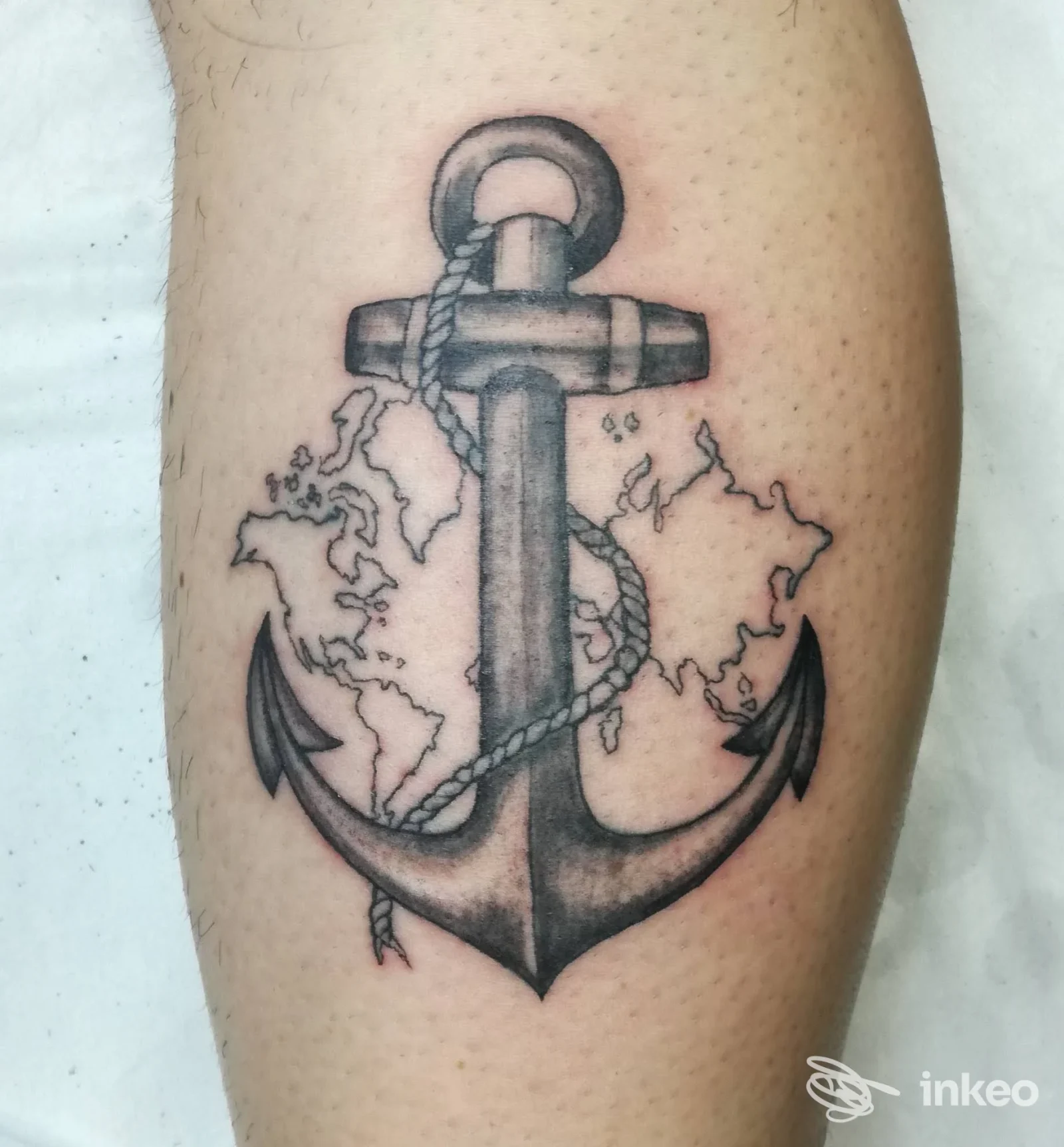 Tatuaggio ancora in nero/grigio su polpaccio con mappa stilizzata del mondo. Immagine da Tattoo'S Studio di Isabella Caddeo, Foligno.