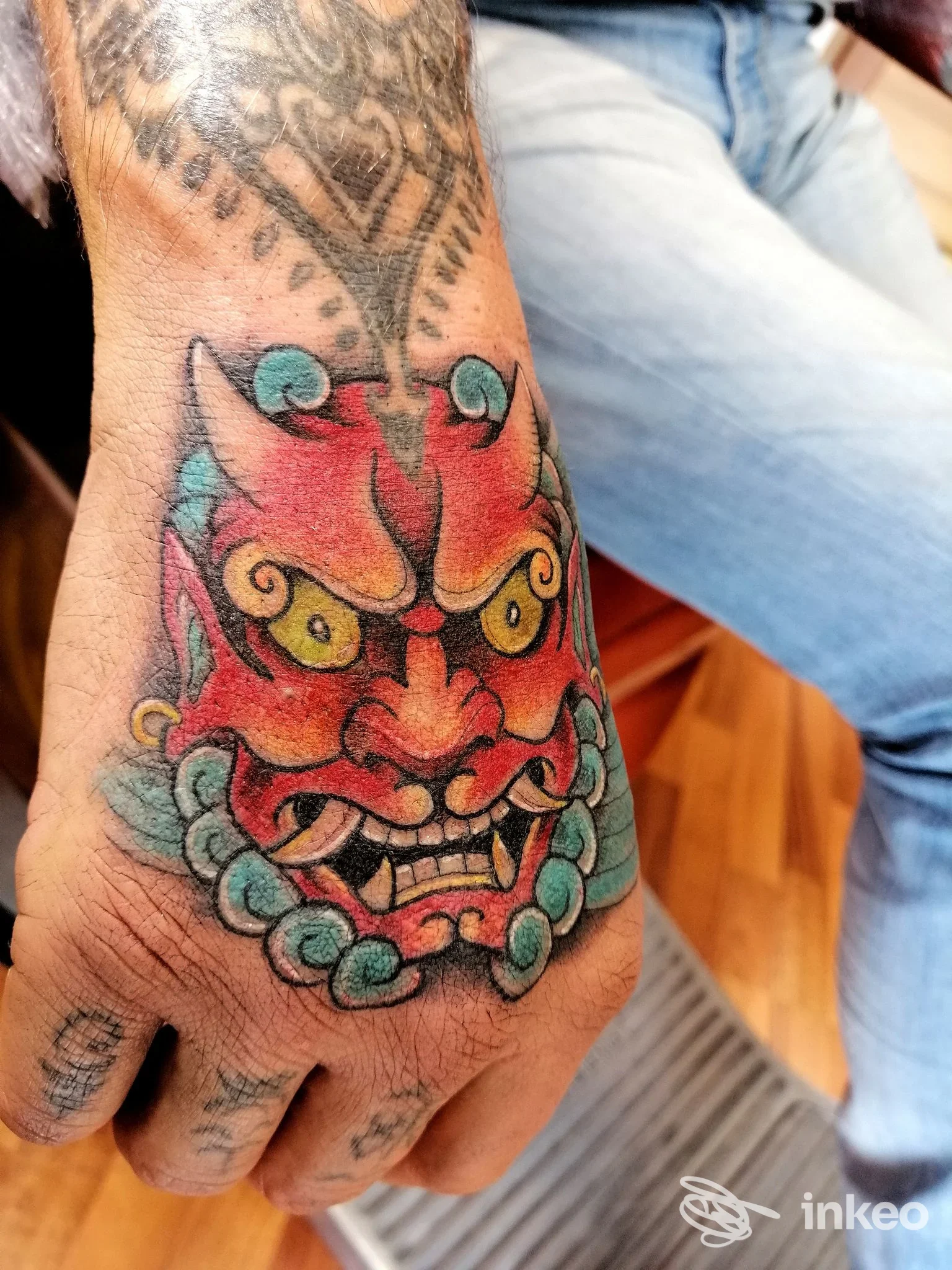 Tatuaggio a colori sul dorso della mano con volto demoniaco e perle turchesi, White Rabbit Tattoo Studio, Perugia.