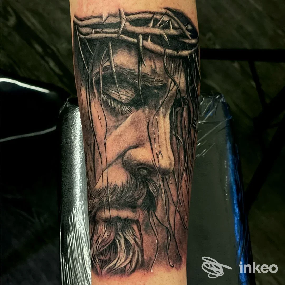 Tatuaggio realistico in bianco e nero di volto religioso sull'avambraccio, realizzato da Bertelli Diego Tattoo ad Aosta.