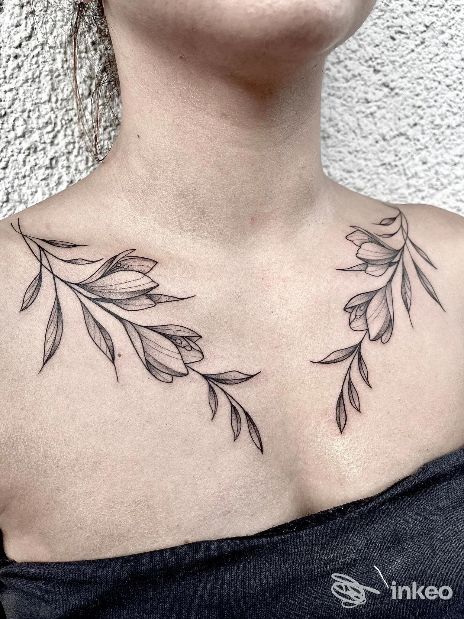 Delicato tatuaggio floreale in nero sulle clavicole e petto superiore, foto ravvicinata con dettagli delle linee. Legend Tattoo Studio, Pont-Saint-Martin.