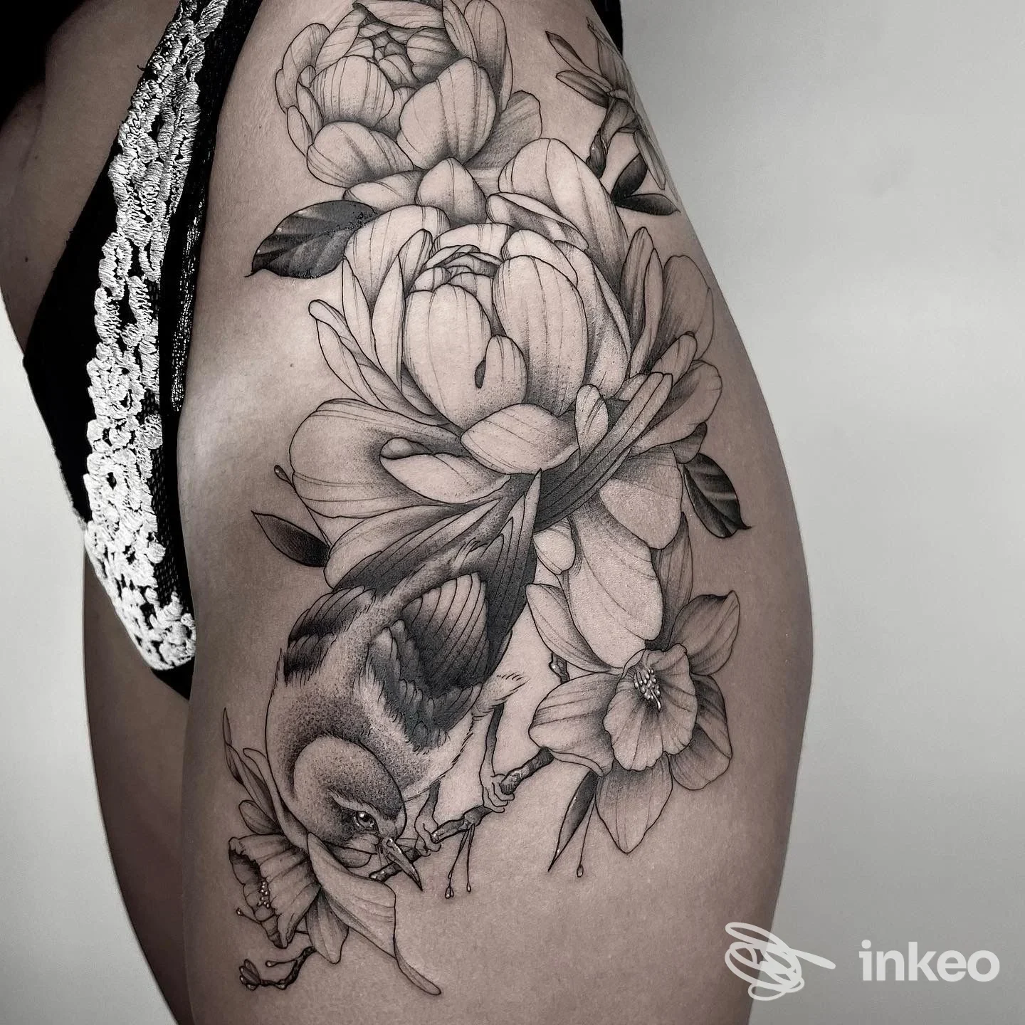 Ampio tatuaggio black & grey di fiori e un uccello su coscia/anca, realizzato da TOMMY blacktattoo ad Aosta.