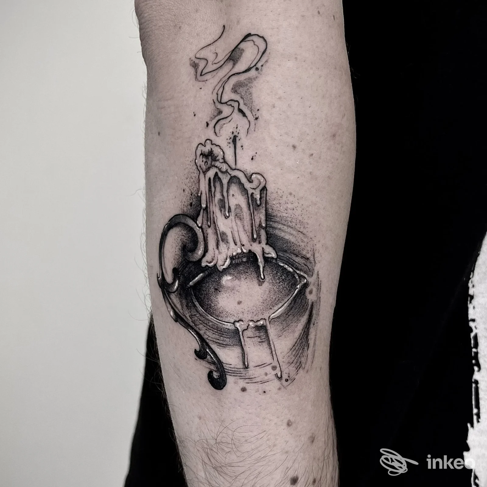 Tatuaggio sull'avambraccio con una candela sciolta che cola in una tazza, linee nere e sfumature grigie, eseguito da TOMMY blacktattoo ad Aosta.
