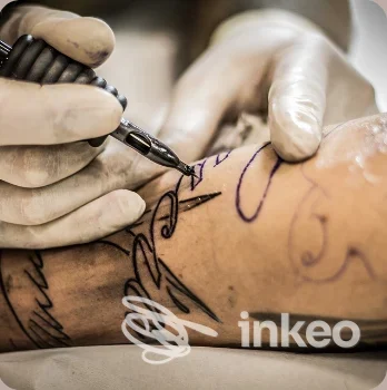 Primo piano di un tatuaggio in corso su avambraccio, operatore con guanti e macchinetta; Tattoo studio Ink Dome, Nus.