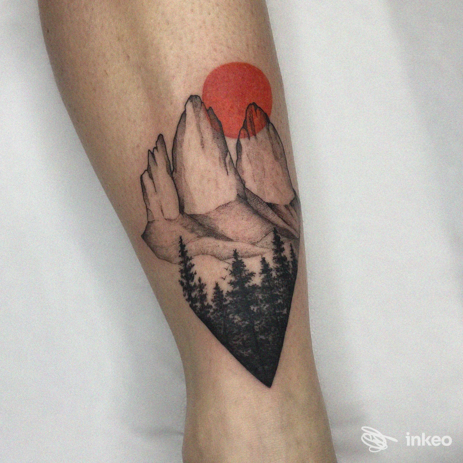 Tattoo sul polpaccio raffigurante paesaggio montano con alberi e sole rosso all'orizzonte, stile realistico/linework, realizzato sulla pelle.