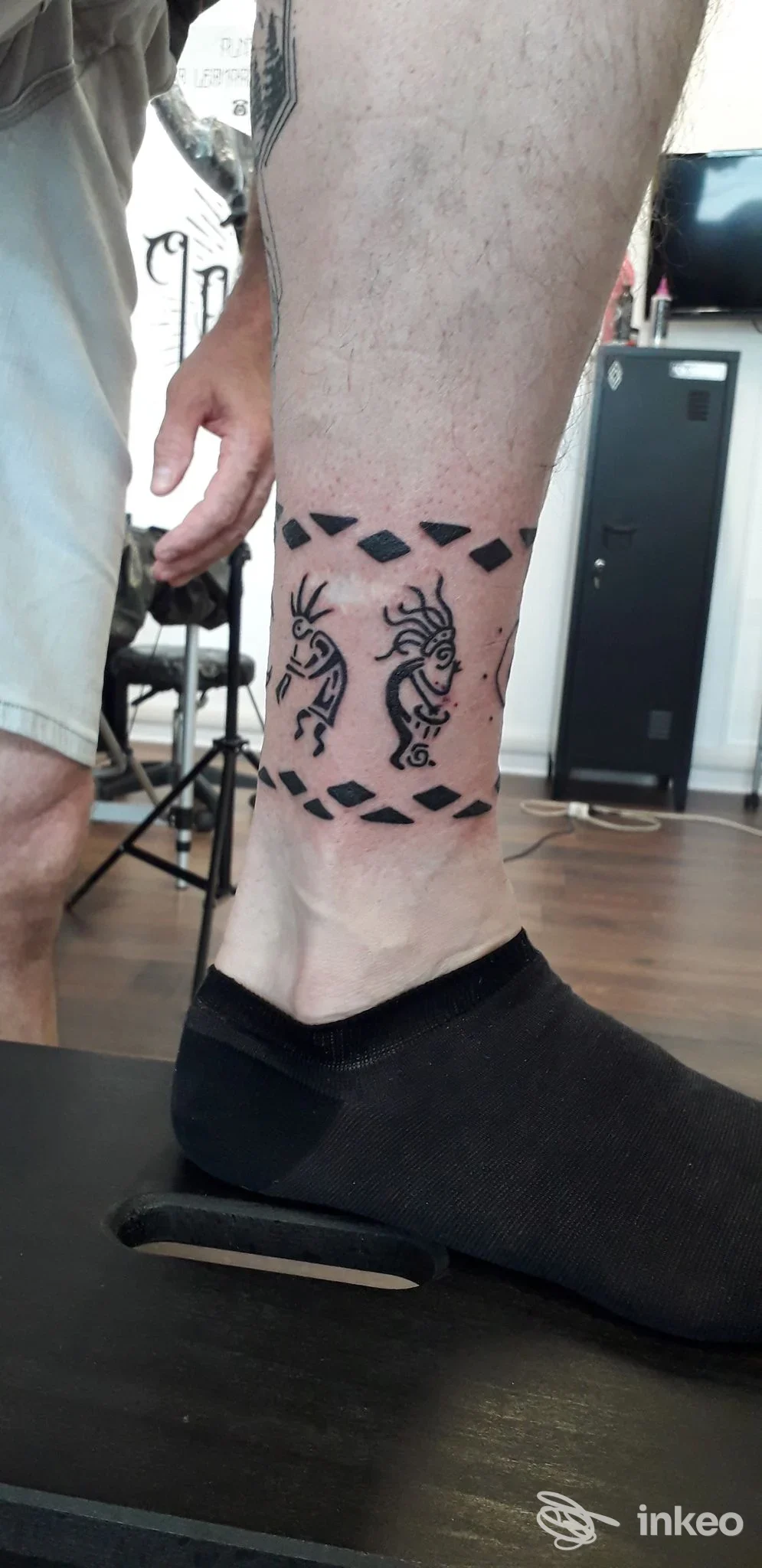 Due tatuaggi stilizzati simmetrici ai lati della caviglia, con una fascia a triangoli neri sopra e sotto, su pelle reale.