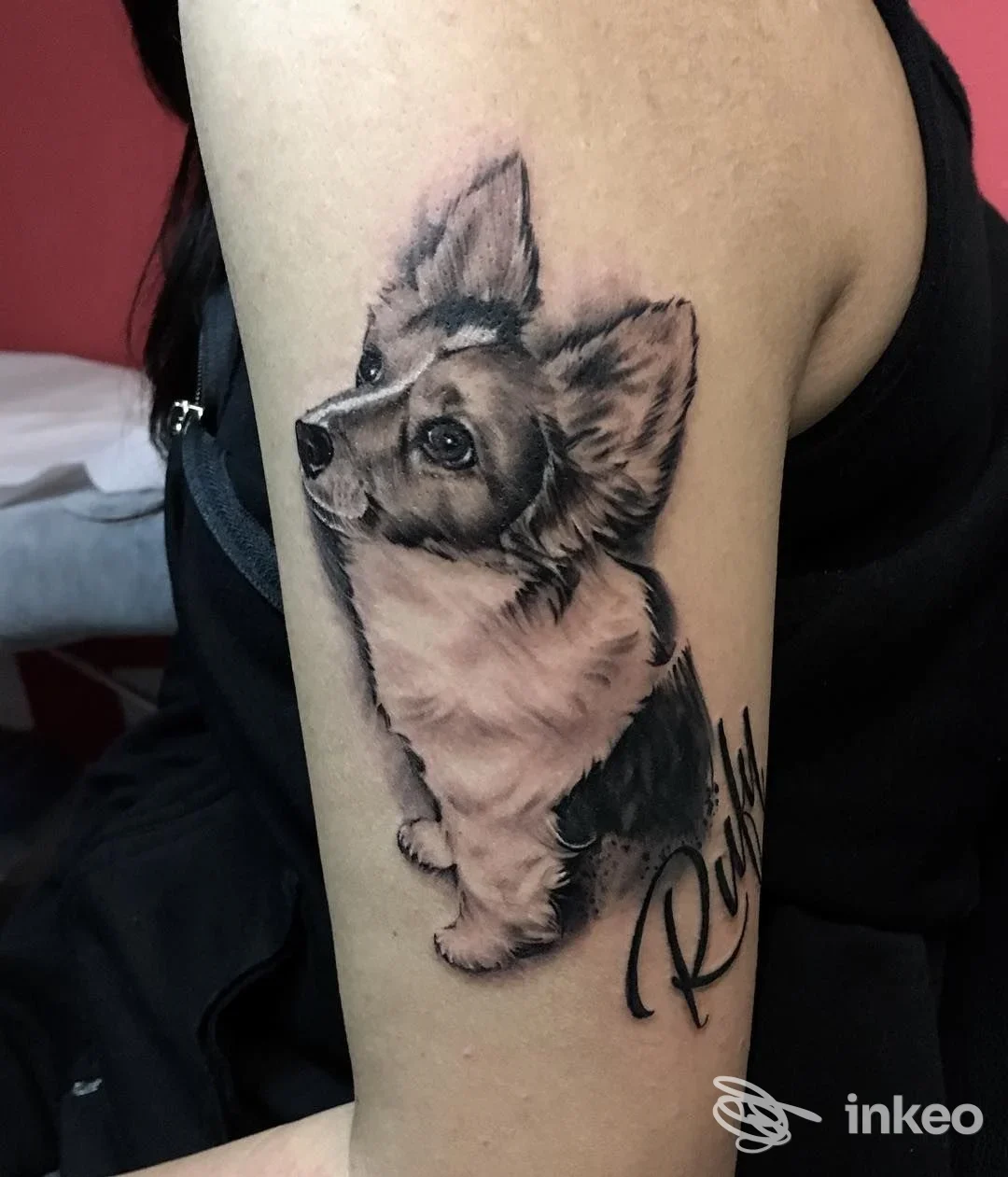 Tattoo realistico di un cane sul braccio, realizzato sulla pelle, firma laterale visibile.