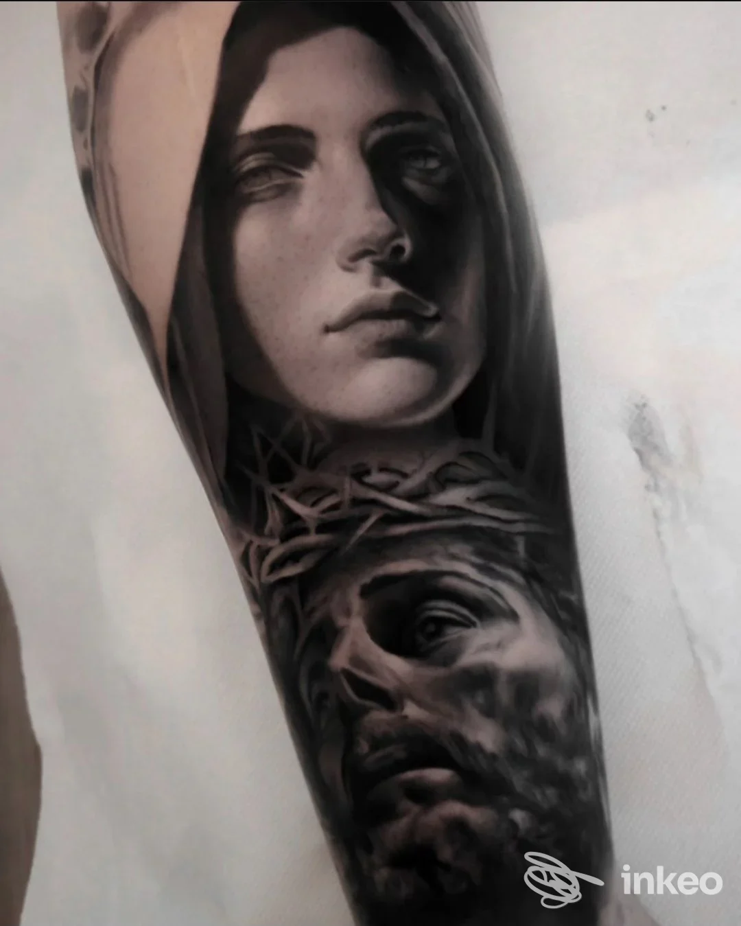 Tattoo visibile sull’avambraccio: ritratto con cappuccio e figura in basso intrecciata da spine, realizzato direttamente sulla pelle.