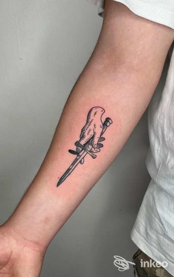 Primo piano di un tatuaggio sul lato interno dell'avambraccio raffigurante una mano con un pugnale, foto per Black Sail Tattoo Studio, Belluno.