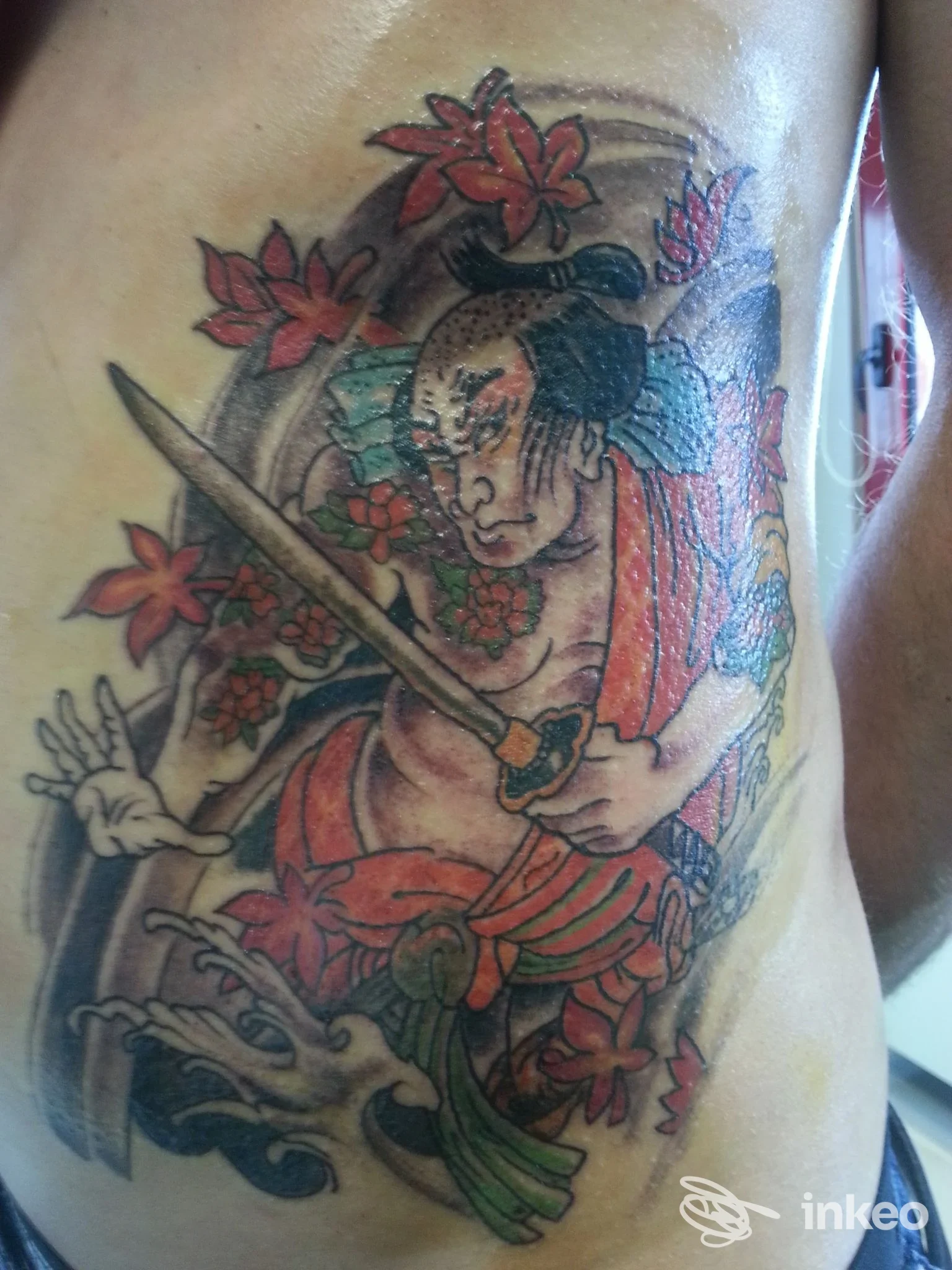 Tatuaggio colorato su fianco/torace destro realizzato da Bonvi Tattoo Studio a Silea, figura armata con fiori e onde.