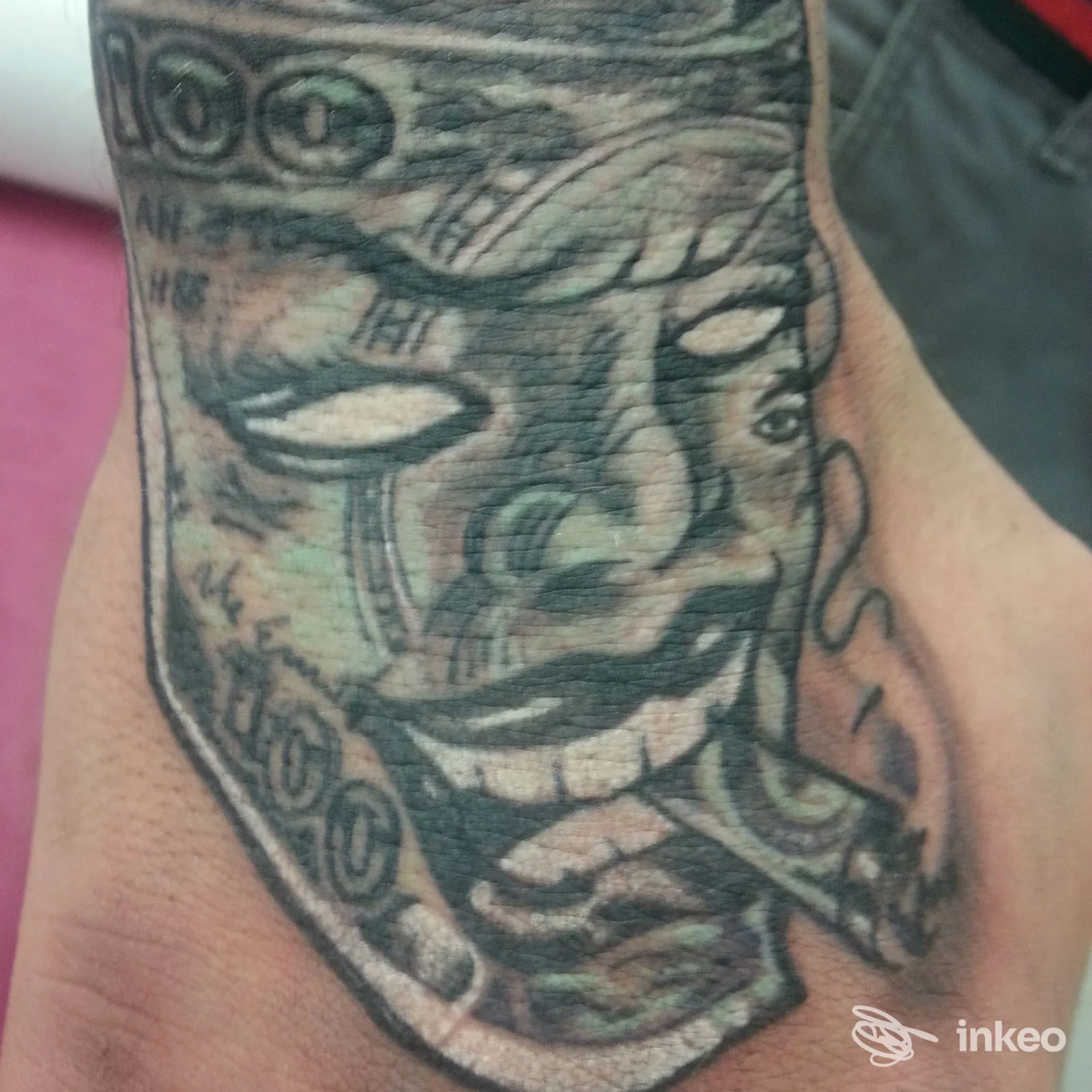 Tatuaggio sul dorso della mano raffigurante un volto con sigaro e banconote, immagine fornita da Bonvi Tattoo Studio a Silea.