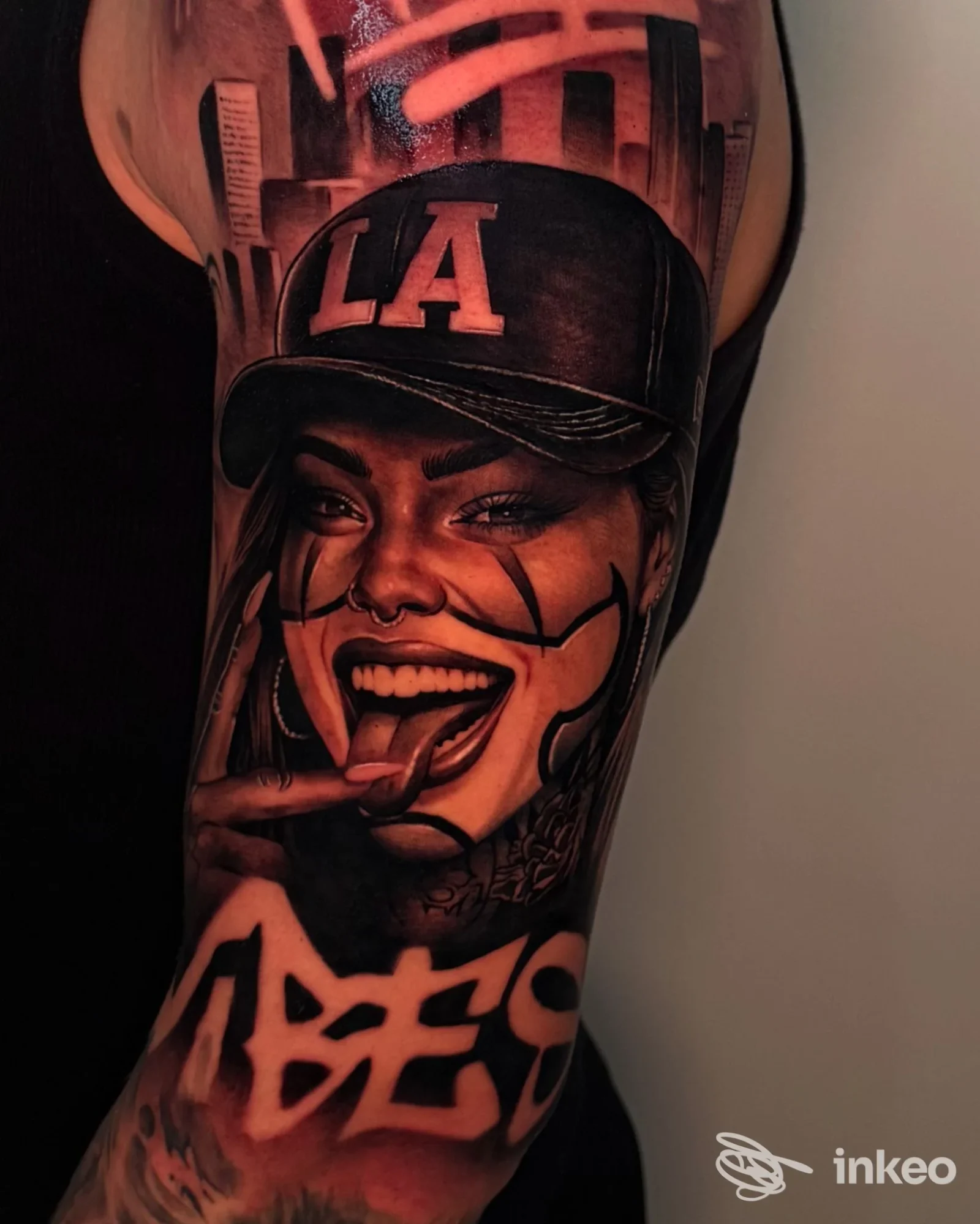 Tatuaggio realistico a colori sul braccio superiore: ritratto femminile con cappellino 'LA' e scritta graffiti. BOG Tattoo, Santa Giustina in Colle.