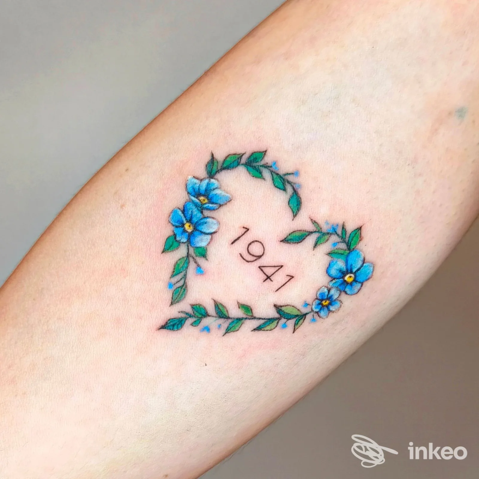 Tatuaggio a forma di cuore con fiori blu e foglie verdi e la cifra 1941 sull'avambraccio, foto fornita da Caterina tattoo a Codiverno.