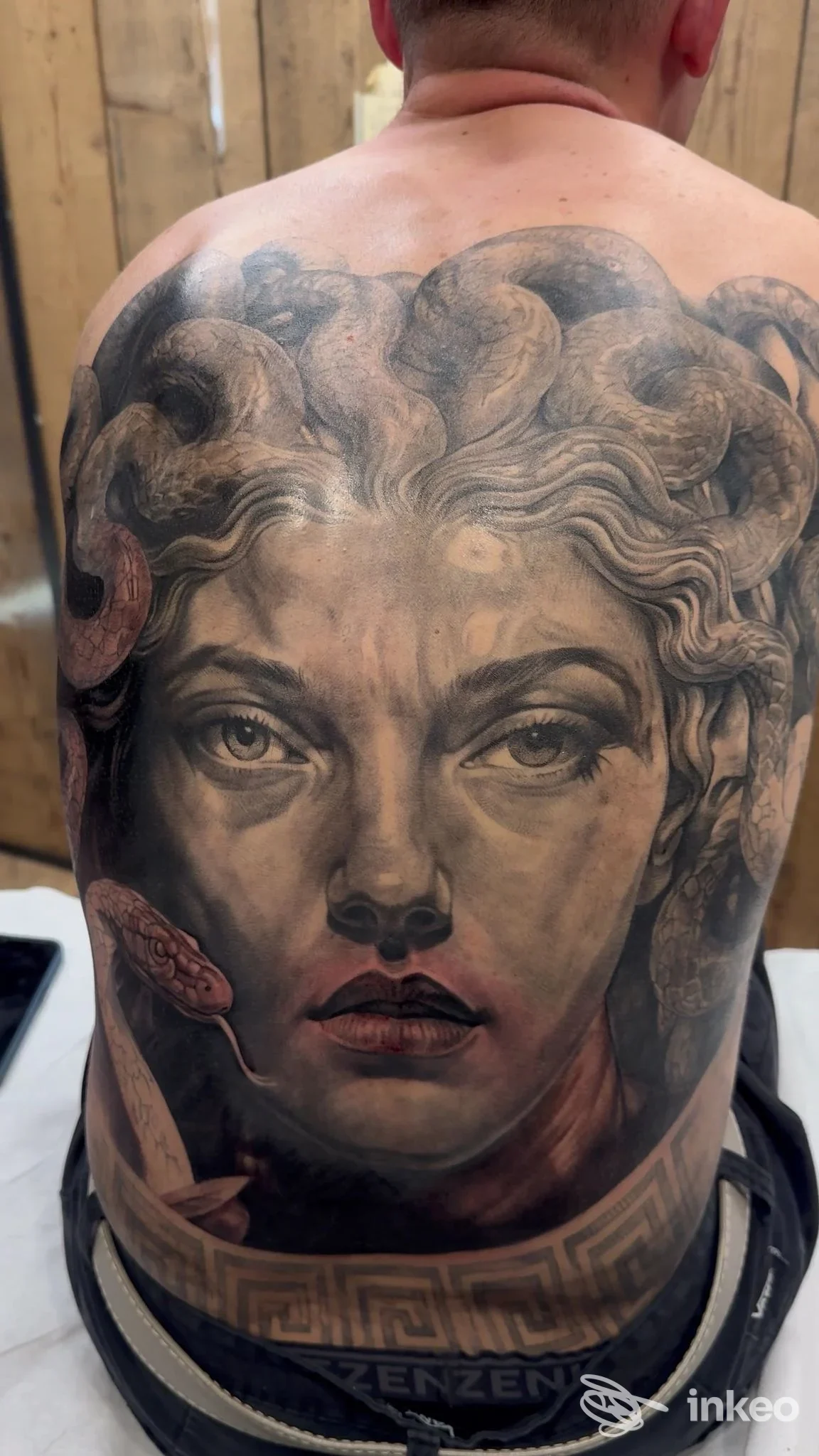 Ampia schiena tatuata con grande ritratto femminile realistico e dettagli di serpenti, lavoro di Cerbero Family Tattoo Studio a Treviso.