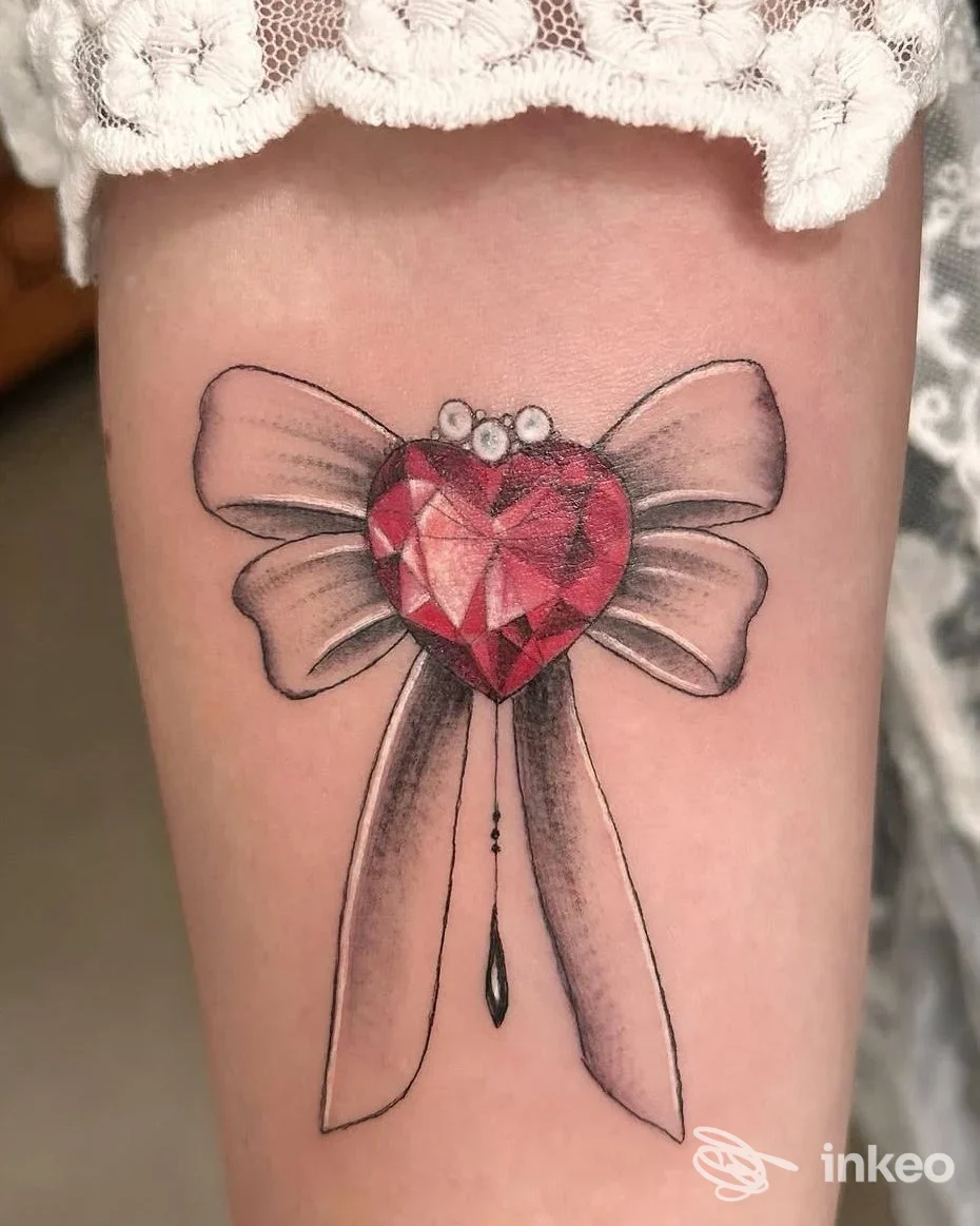 Tatuaggio sull'avambraccio: fiocco con gemma a cuore rosso e ombreggiature grigie. ColorBlind Tattoo Piercing Studio, Padova.