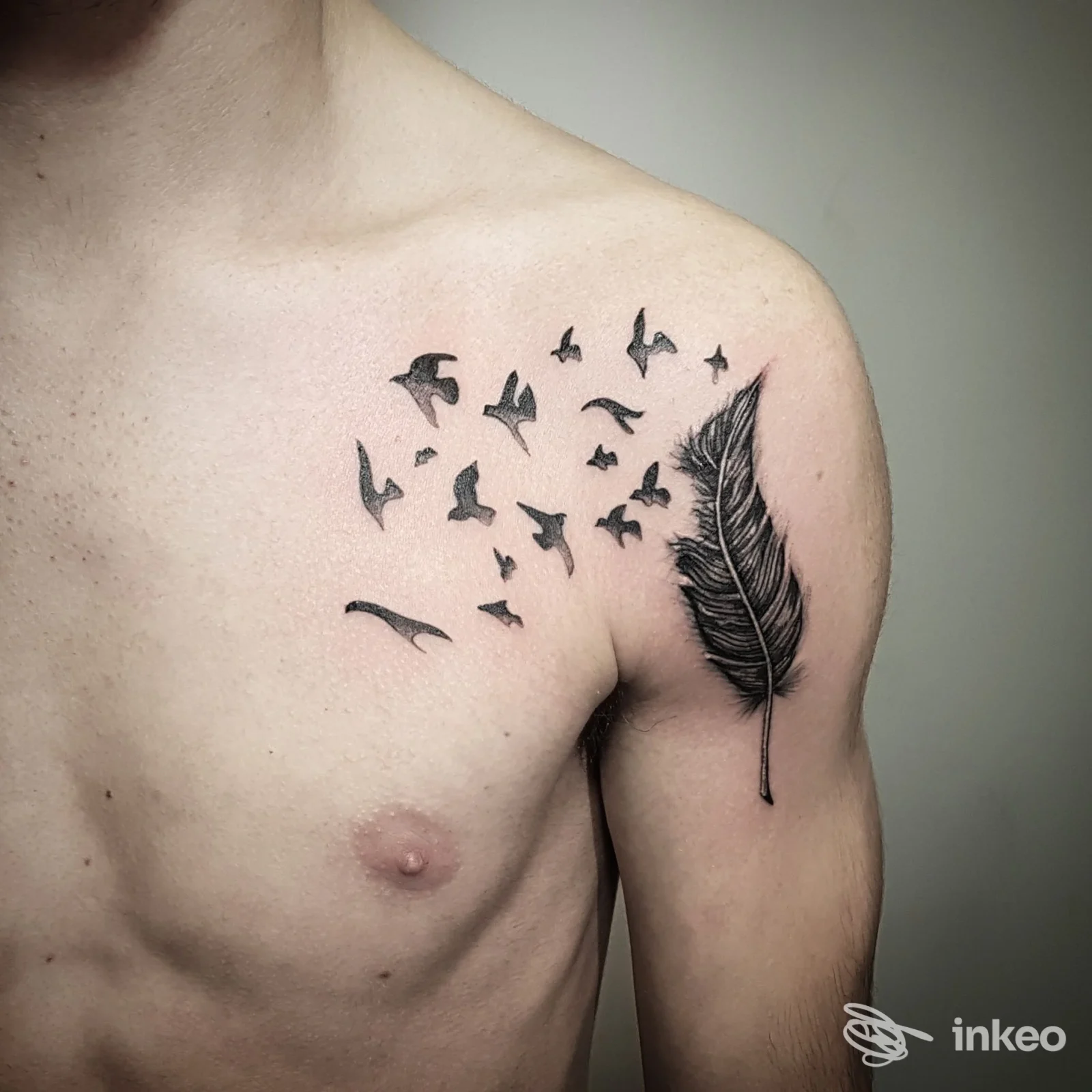 Tatuaggio a inchiostro nero: piuma sulla spalla con stormo di uccelli che si allontana sul petto, realizzato da DEMON - Piercing & Tattoo a Verona.