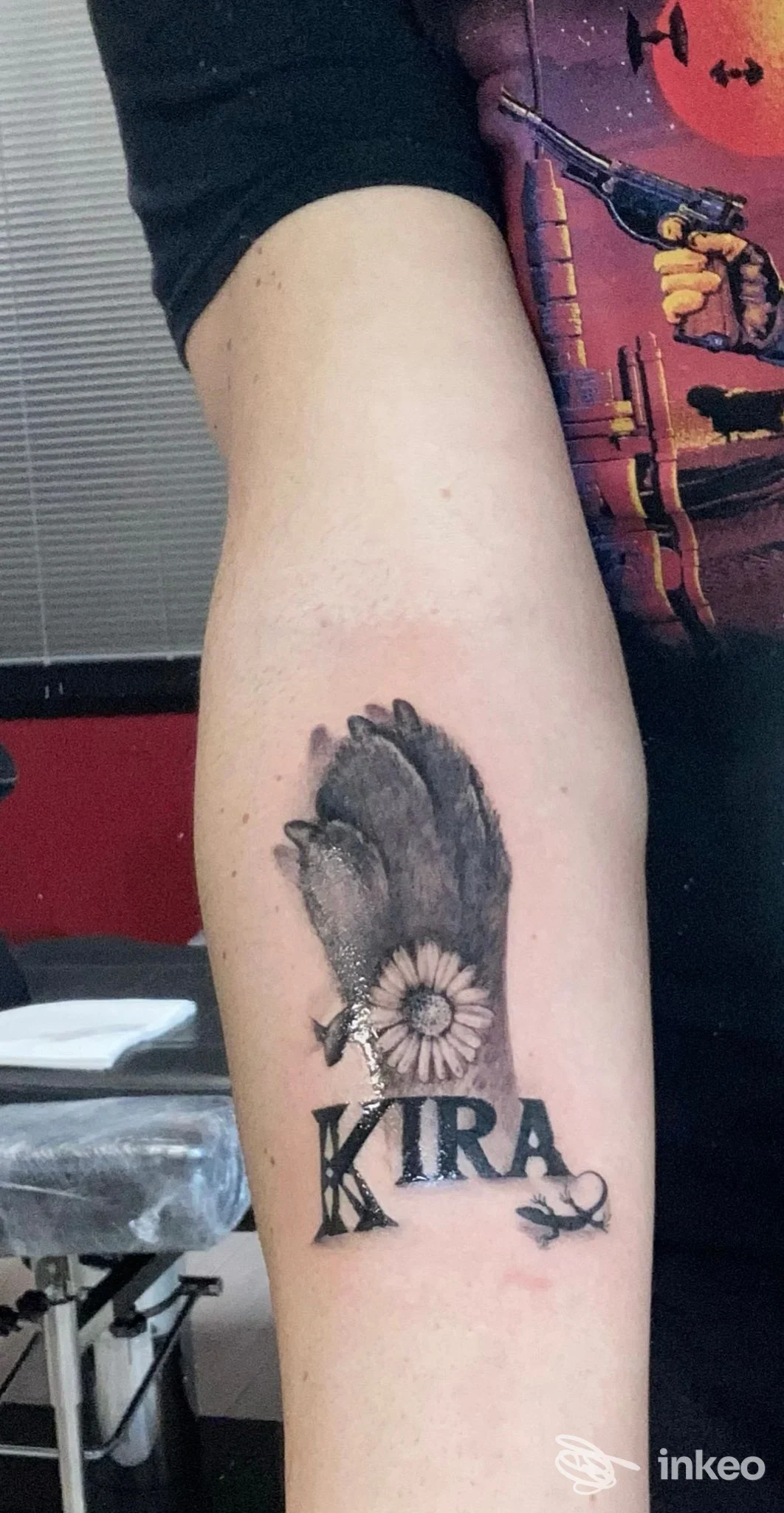 Tatuaggio su avambraccio con ala, margherita e la scritta 'KIRA' — DOUBLE SHOT Tattoo Experience, Ponte San Nicolò.