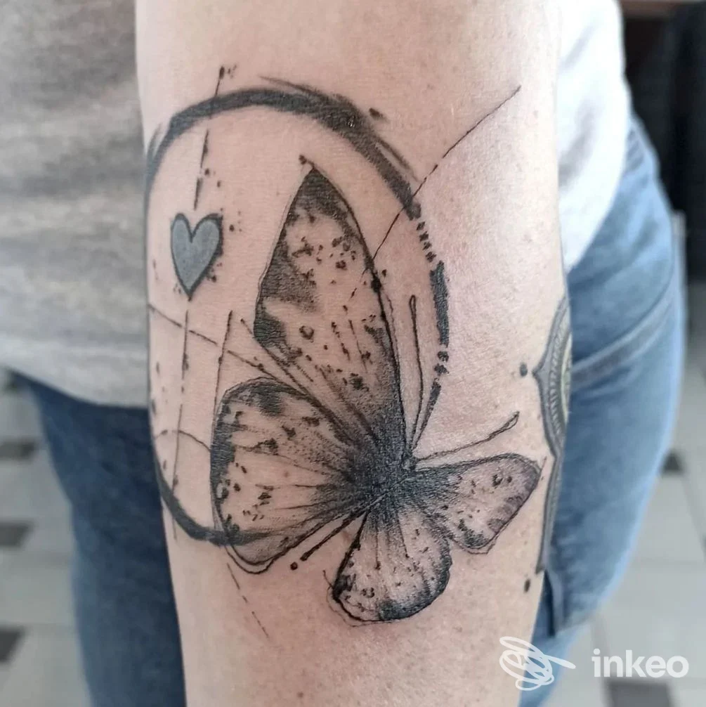 Farfalla nera sfumata con piccolo cuore su avambraccio, tatuaggio fotografato da DELIRIO TATTOO AND GALLERY a Camisano Vicentino.