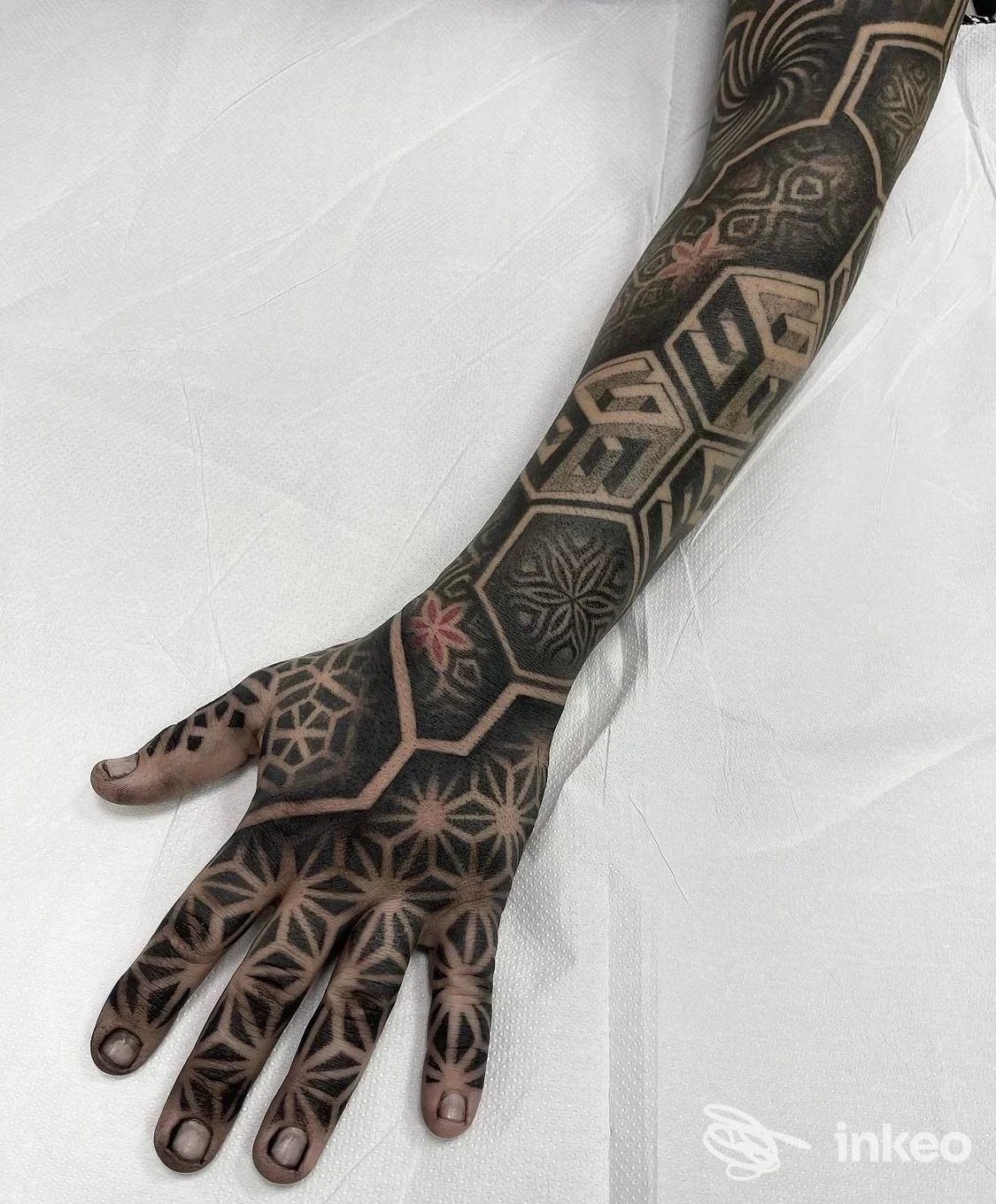 Avambraccio e mano tatuati con motivi geometrici e accento rosso, foto fornita da Dark Mind Tattoo Studio a Meledo.