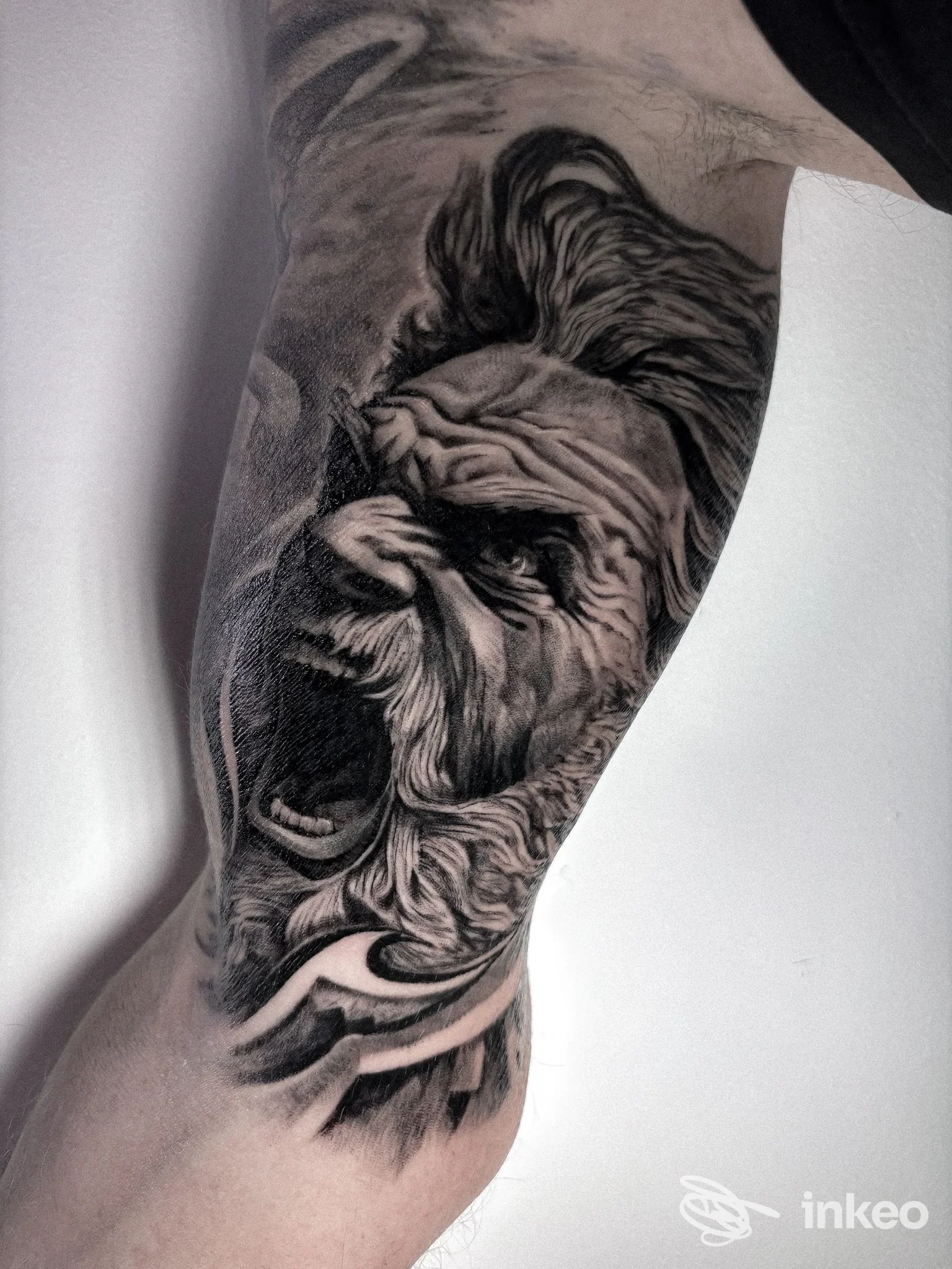 Tatuaggio realistico in bianco e nero di un volto ruggente sull'interno del bicipite. Foto fornita da DryInk Tattoo, Selvazzano Dentro.