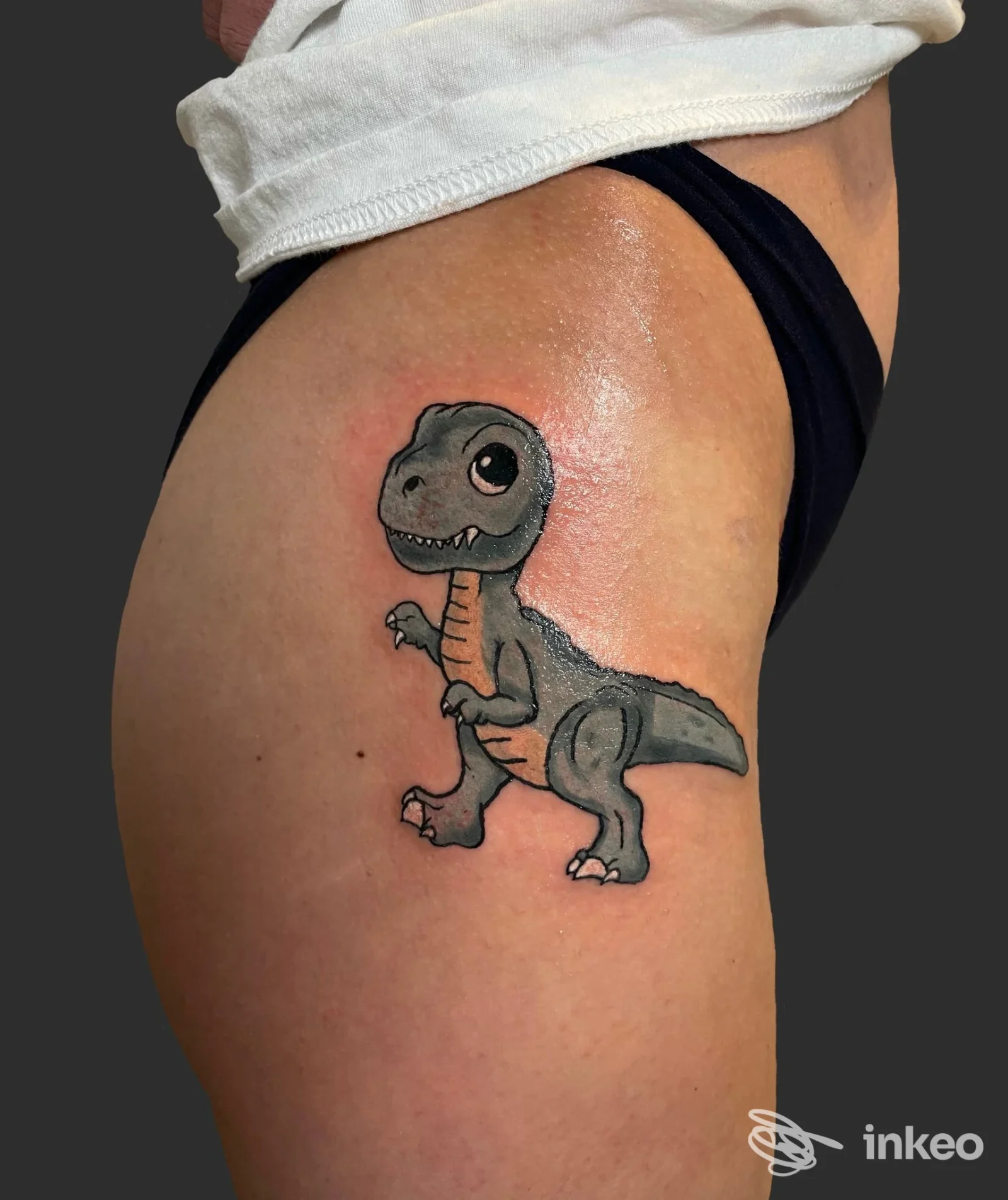 Tatuaggio di un piccolo dinosauro in stile cartoon sulla coscia, realizzato presso First Order Tattoo Studio, Padova.