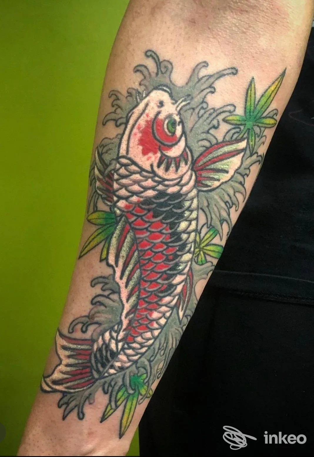 Tatuaggio di koi giapponese su avambraccio, con squame rosse e nere, contorno nero e accenni verdi delle foglie, realizzato su pelle. Studio Primordial Pain, Milano.