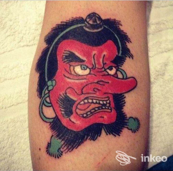 Tattoo colorato su pelle: volto di demonio rosso con capelli neri, orecchie e accessori verdi, realizzato a Primordial Pain a Milano.