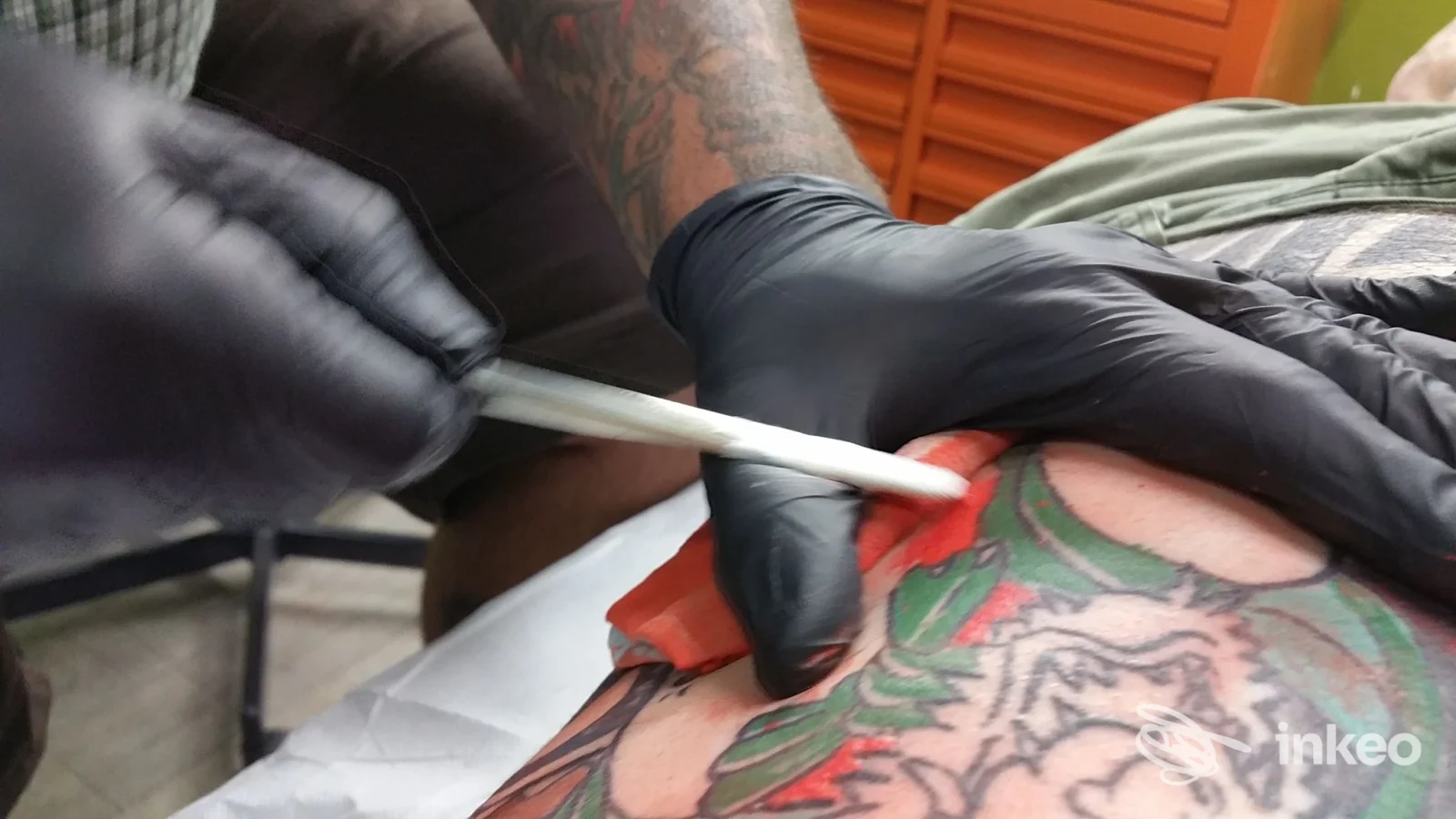 Primo piano su una sessione di tatuaggio: mani con guanti neri utilizzano lo strumento su una pelle già tratteggiata, nessun volto visibile, studio Primordial Pain a Milano.