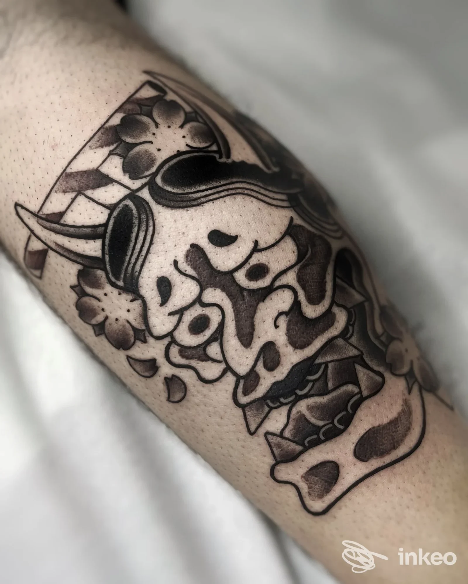 Tatuaggio nero e grigio raffigurante una maschera stilizzata con fiori sull'avambraccio, Flow Tattoo Studio, Camposampiero.