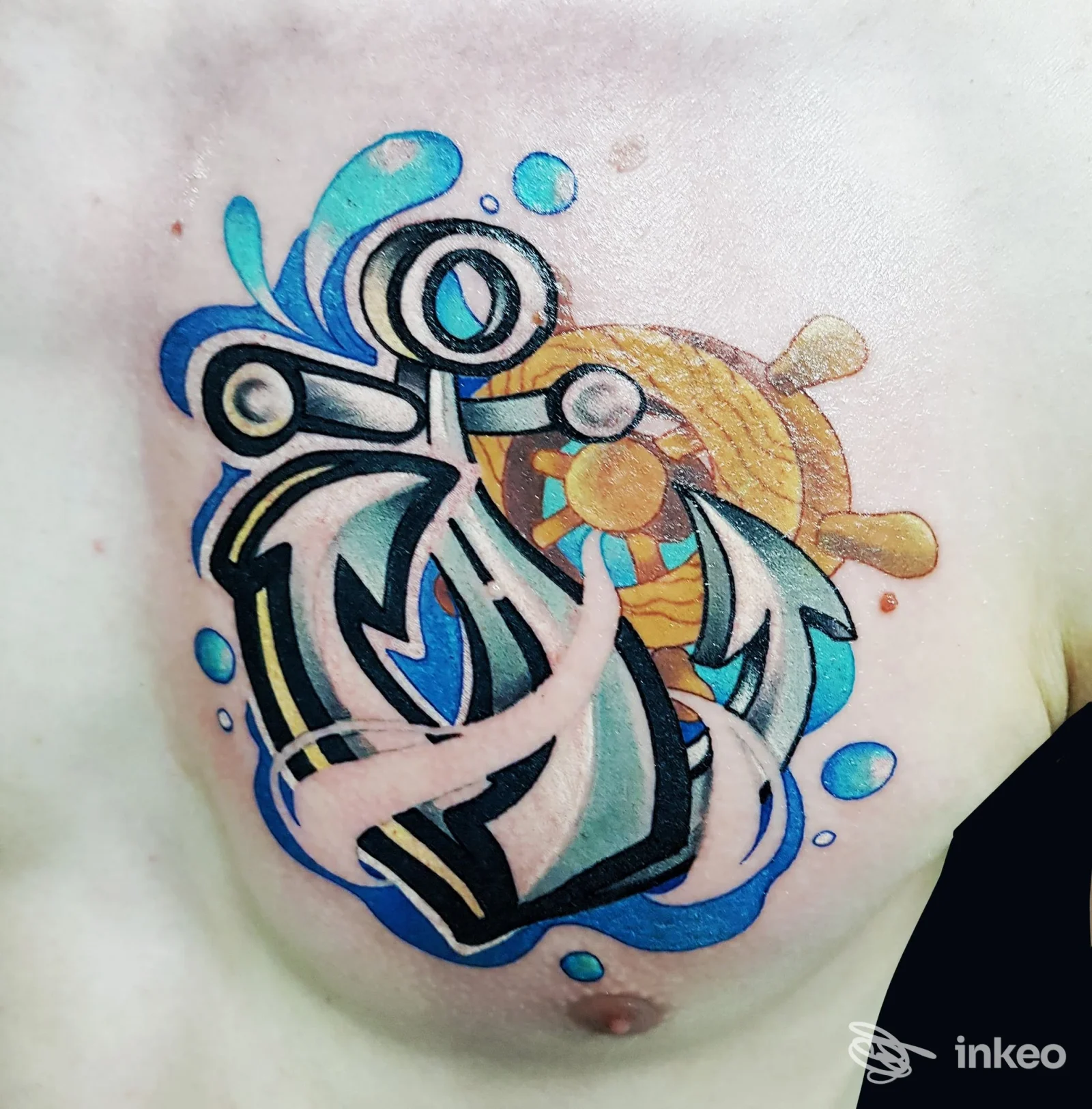 Tatuaggio colorato con ancora e timone sul petto; lavoro mostrato dallo studio Hostile Tattoo Studio a Feltre.