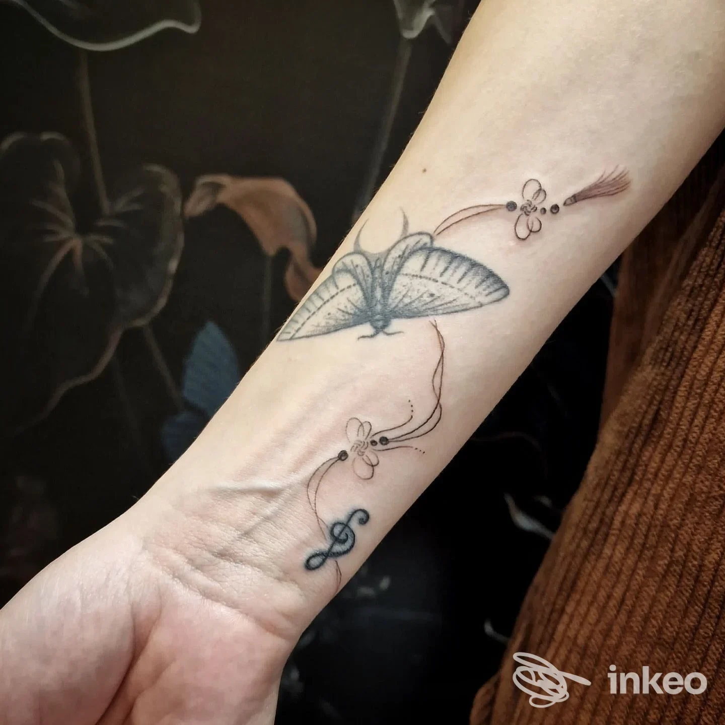 Braccio con tatuaggio in stile linework raffigurante una farfalla stilizzata con fiori, tracciato sottile lungo l’avambraccio, visibile sulla pelle.