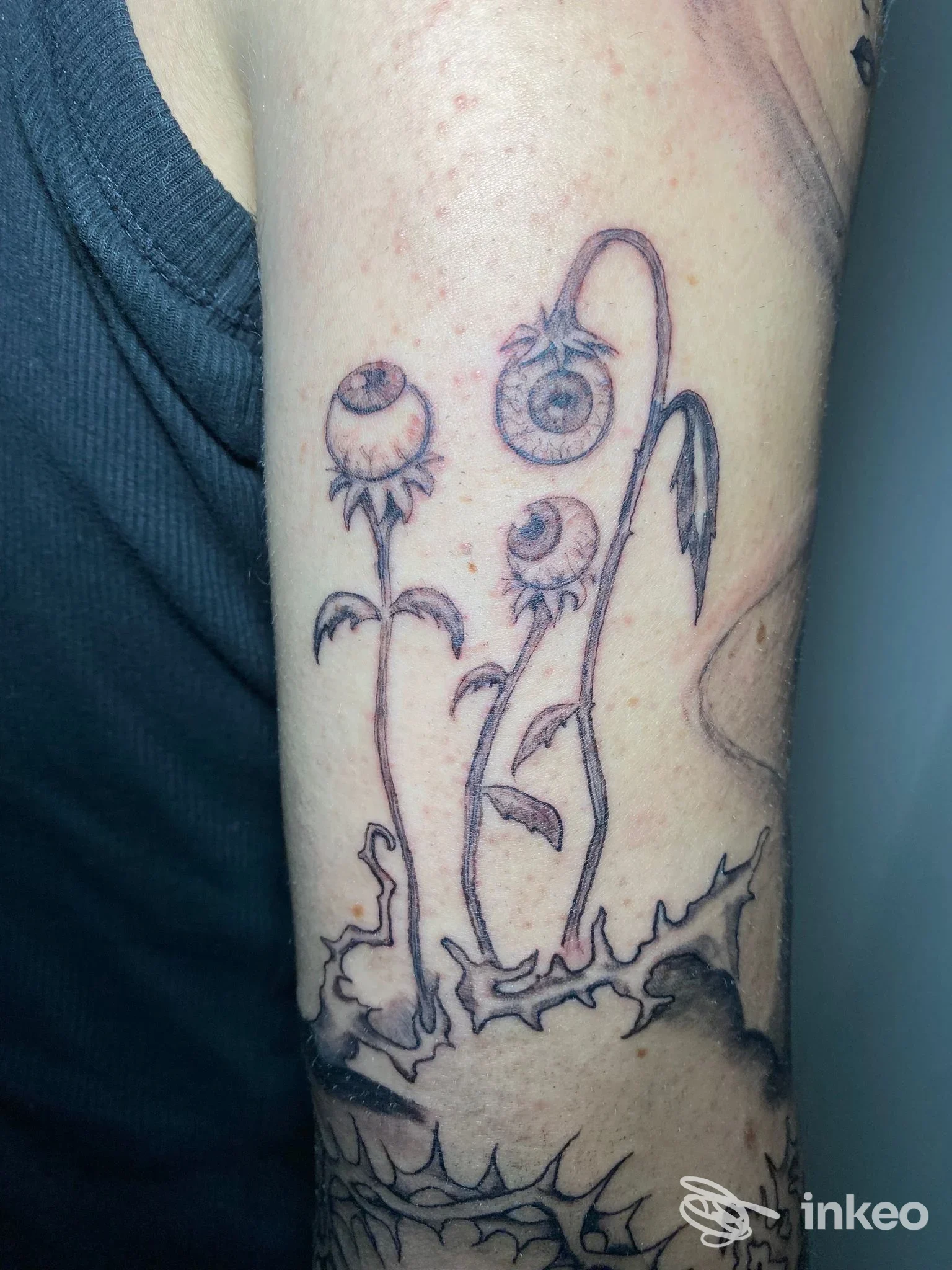 Tatuaggio floreale con occhi su braccio, linework nero e ombreggiature — Infracuor Tattoo & Piercing, Riese Pio X.