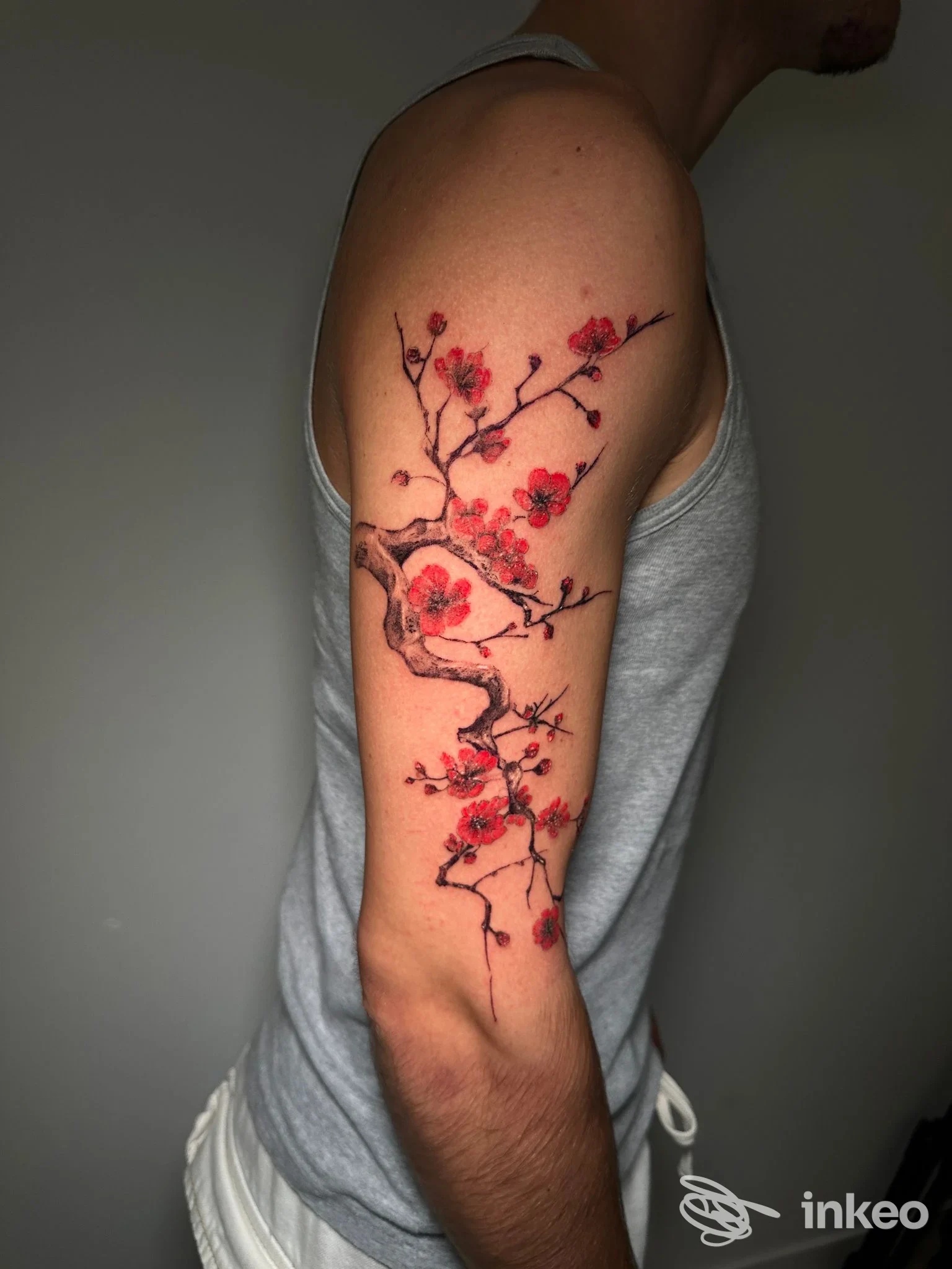 Tatuaggio ramo fiorito rosso e nero sul braccio superiore di una persona con canotta grigia — Invictus Tattoo Company Italy, Preganziol.