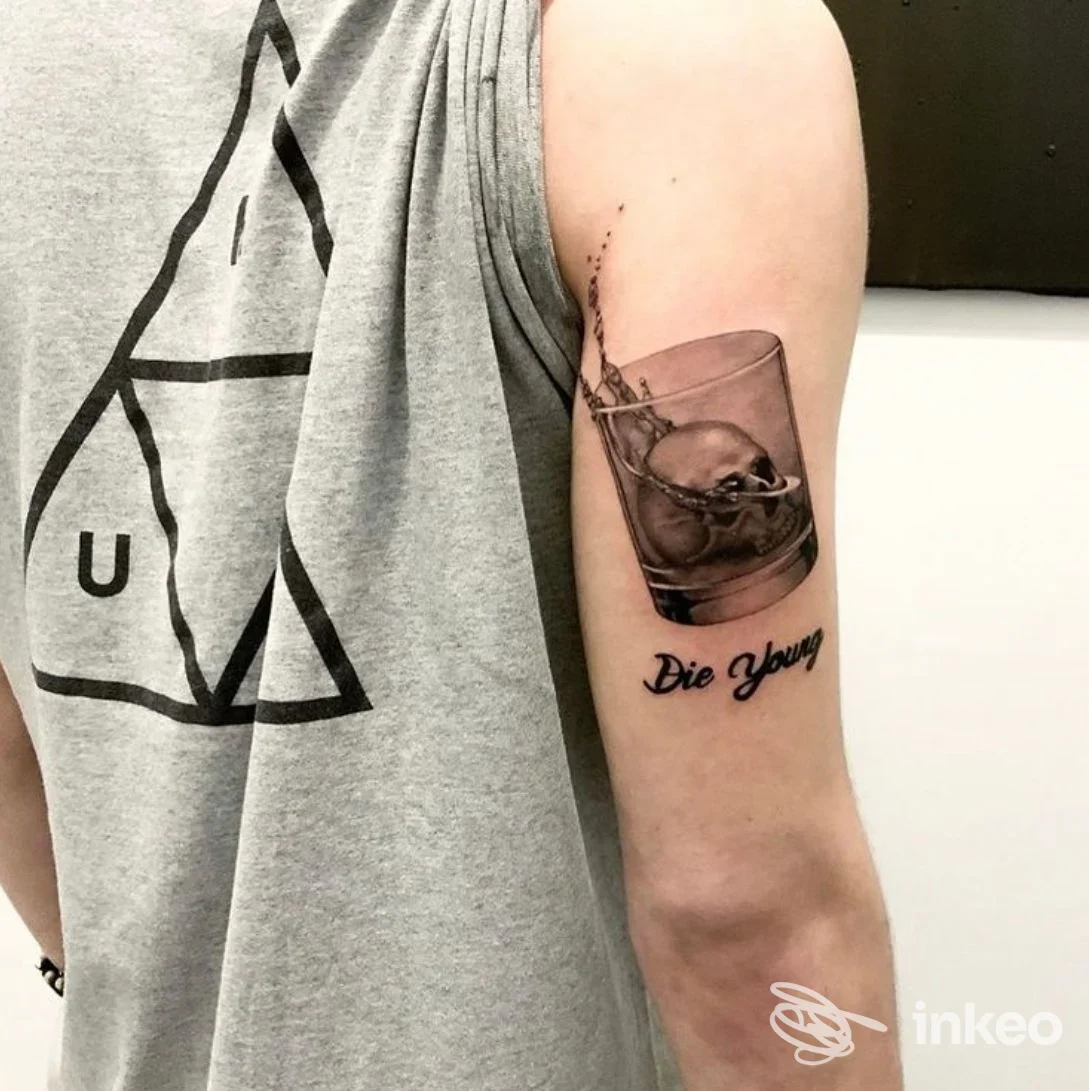 Tatuaggio sulla parte superiore del braccio: teschio in un bicchiere con la scritta 'Die Young', foto dello studio Kamatattoo a Stra.