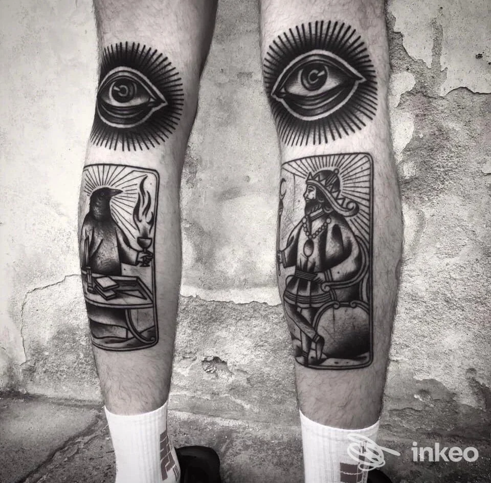 Fotografia in bianco e nero dei polpacci tatuati presso Klinik piercing e tattoo, Treviso: grandi occhi e carte illustrative in stile blackwork.