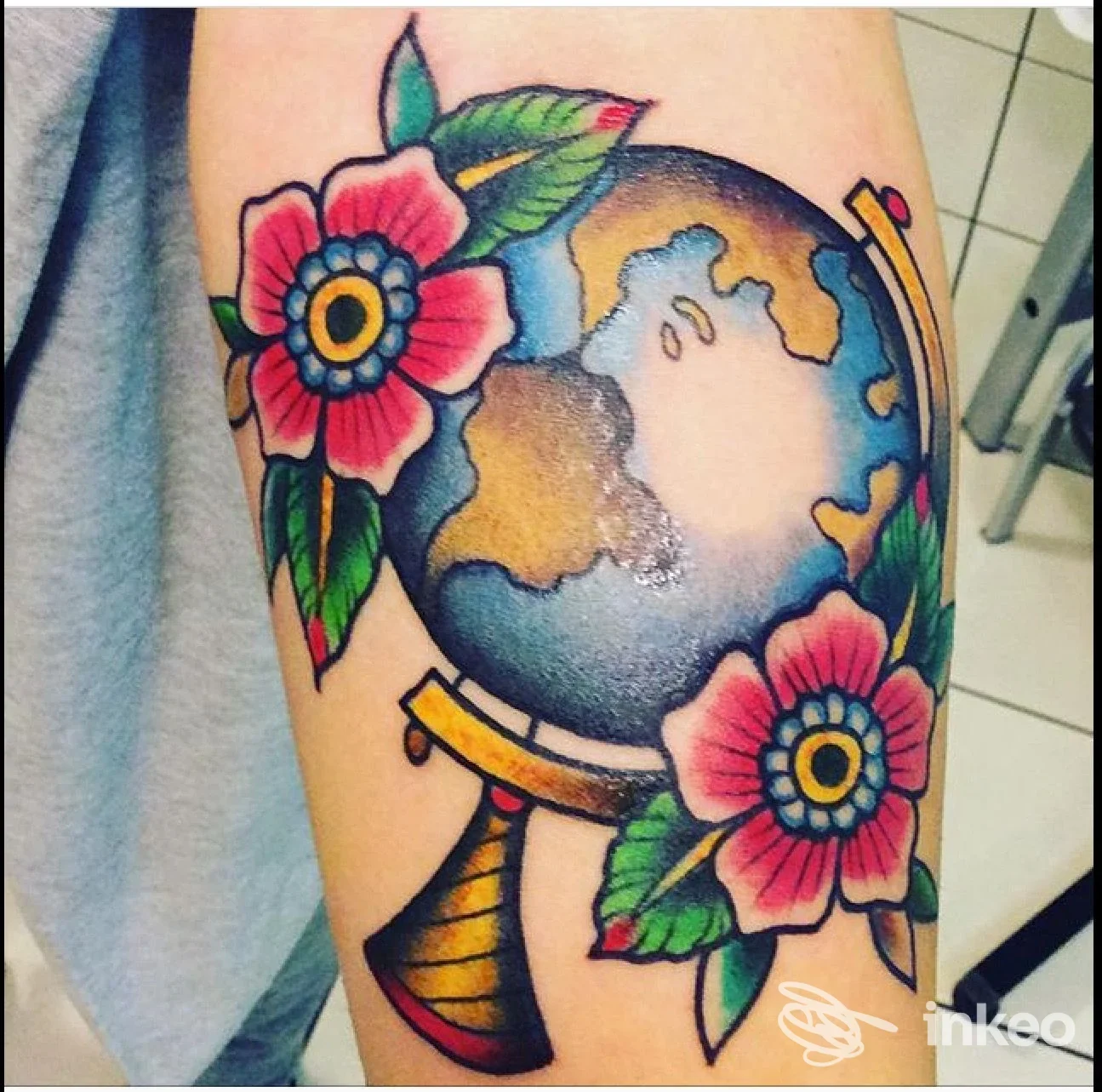 Tatuaggio a Belluno dello studio La Fenice Tattoo & Piercing: mappamondo tradizionale con fiori colorati sull'avambraccio.