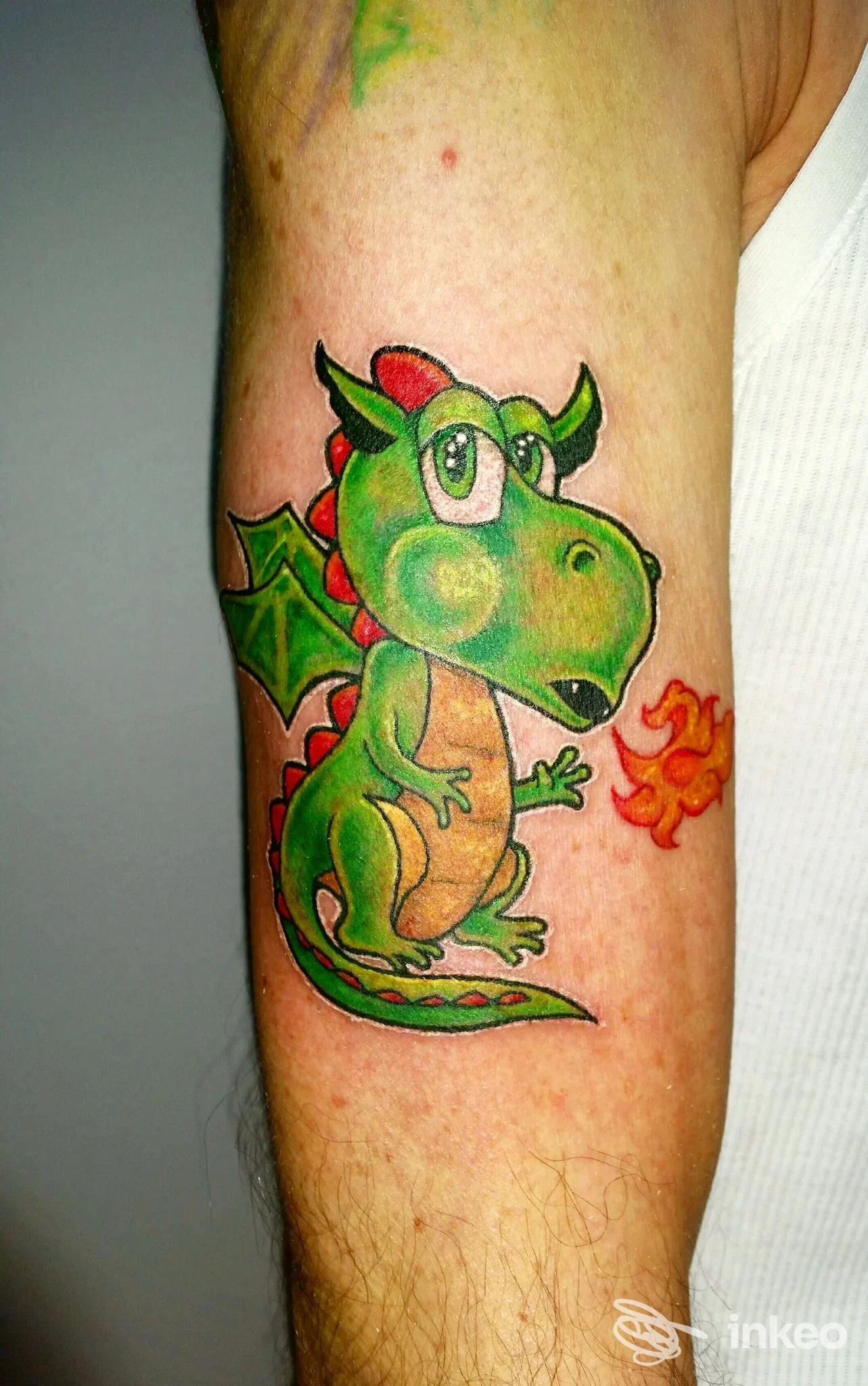 Tatuaggio colorato di un piccolo drago cartoon sull'avambraccio, Living Colors 6 Tattoo & Body Piercing, Castelfranco Veneto.