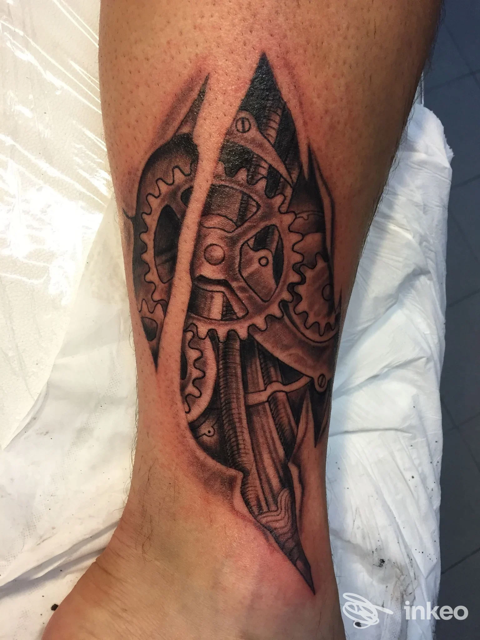 Tatuaggio black & grey con ingranaggi che emergono come lacerazioni sul polpaccio, Macchianera Tattoo Studio, Villorba.
