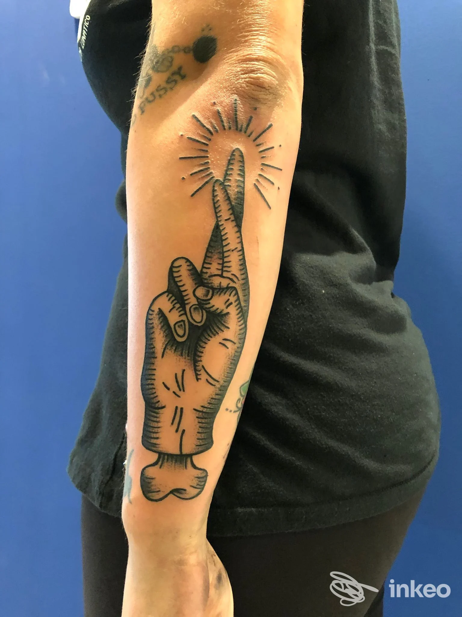Tatuaggio stilizzato di una mano con dita incrociate e raggi luminosi sull'avambraccio destro, fotografia per La Belva tattoo e piercing, Zermeghedo.