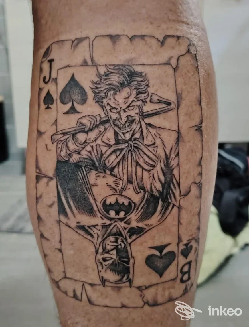 Tatuaggio su polpaccio raffigurante una carta da gioco con Joker e Batman, Mastodon Tattoo Verona, Lugagnano.