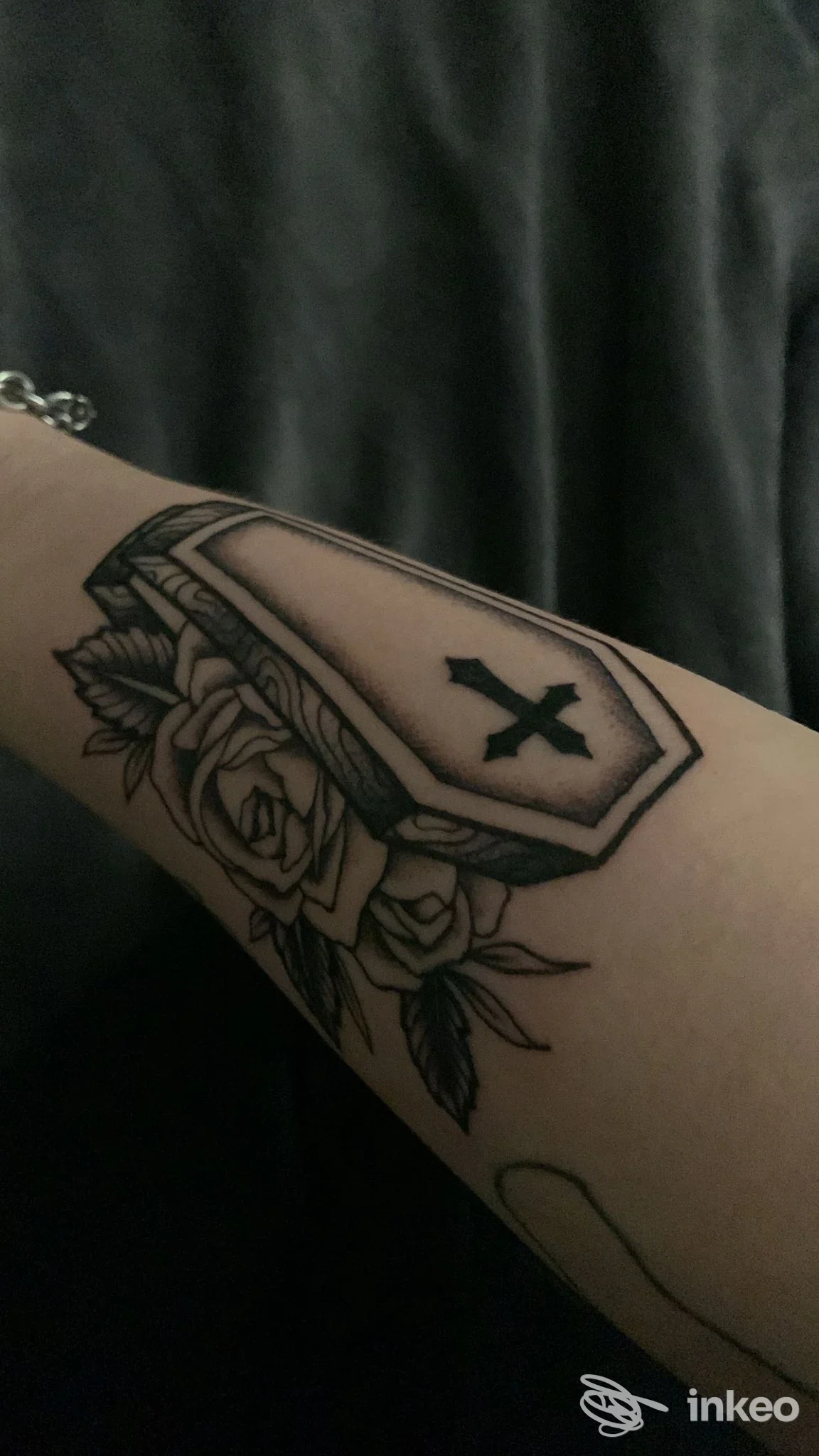 Tatuaggio a inchiostro nero di una bara con croce e rose sull'avambraccio, foto fornita da Octopus Ink Tattoo Studio, Padova.