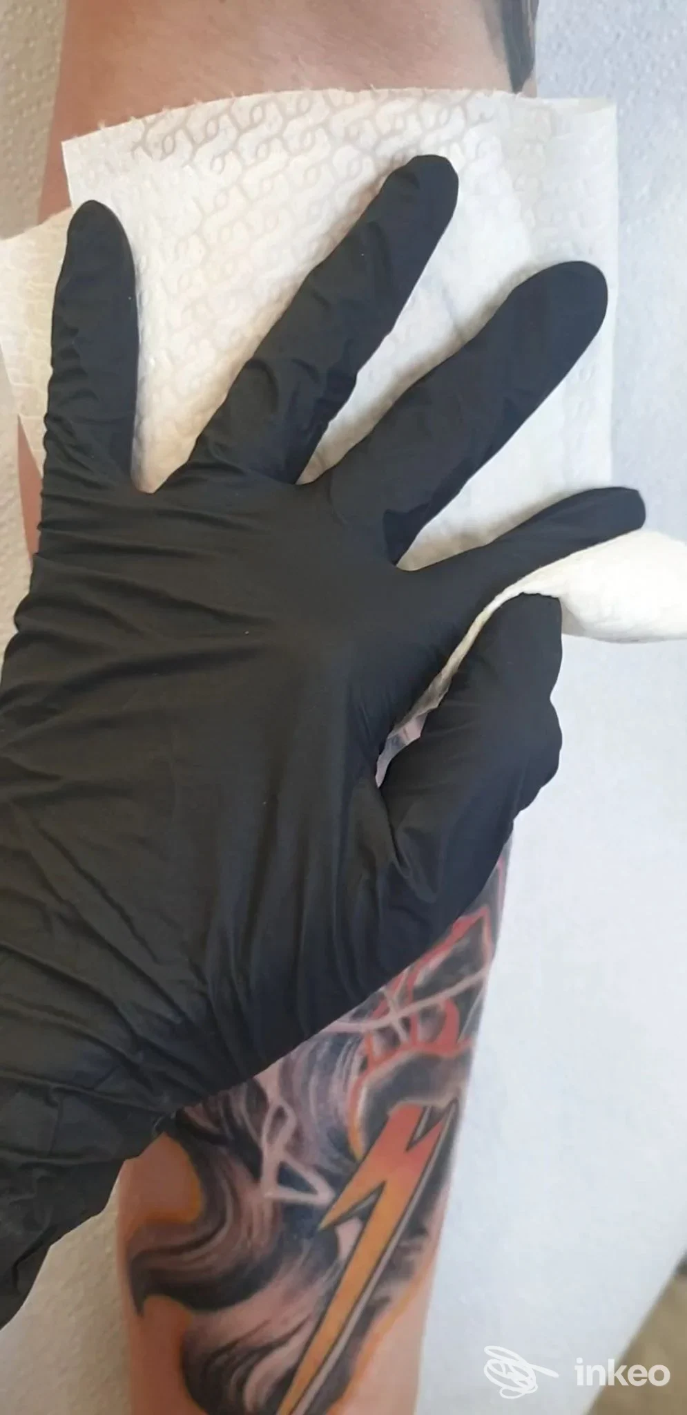 Mano guantata che solleva una salvietta mentre viene mostrato un tatuaggio colorato sull'avambraccio. Octopus Ink Tattoo Studio, Padova.