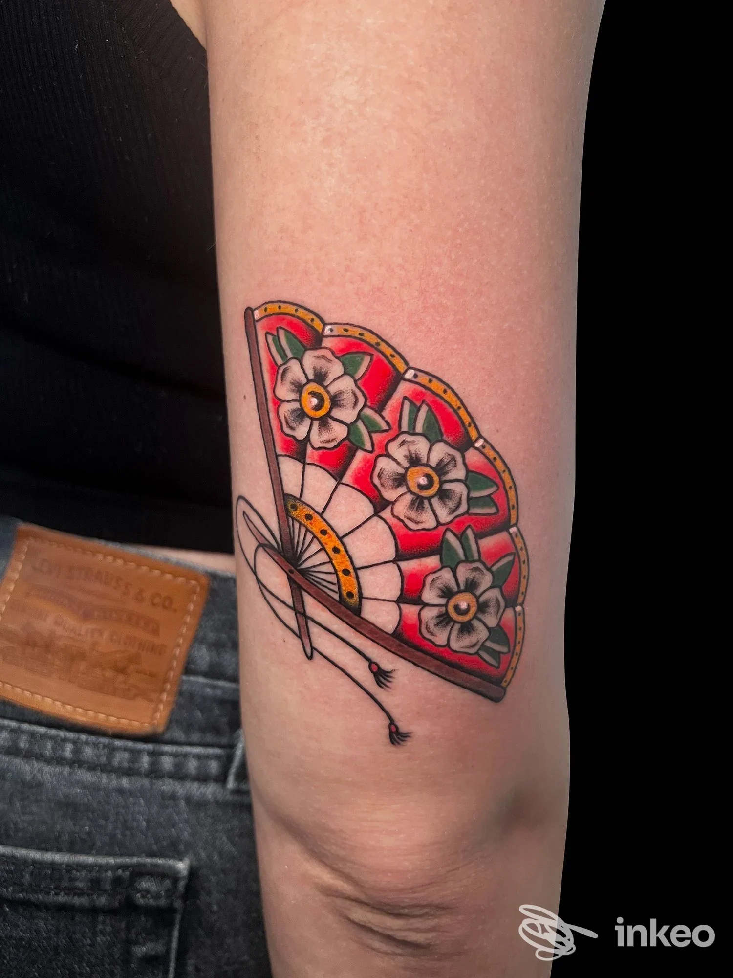Tattoo a colori su avambraccio raffigurante un ventaglio ornato di fiori. descrizione fedele dell’immagine. Ligera Ink Tattoo, città non indicata.