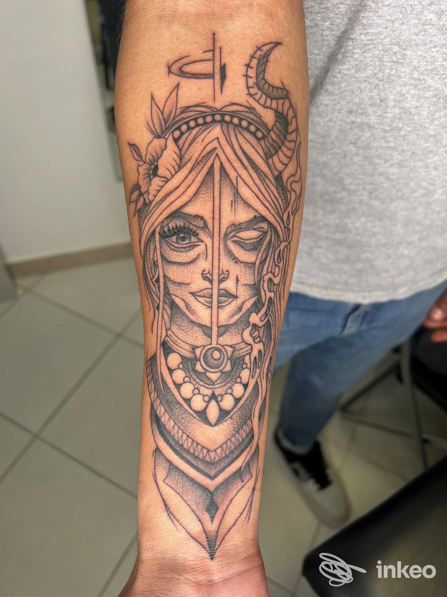 Tatuaggio in bianco e nero su avambraccio con volto stilizzato, corna e motivi ornamentali. Mantra Tattoo Studio, Este.