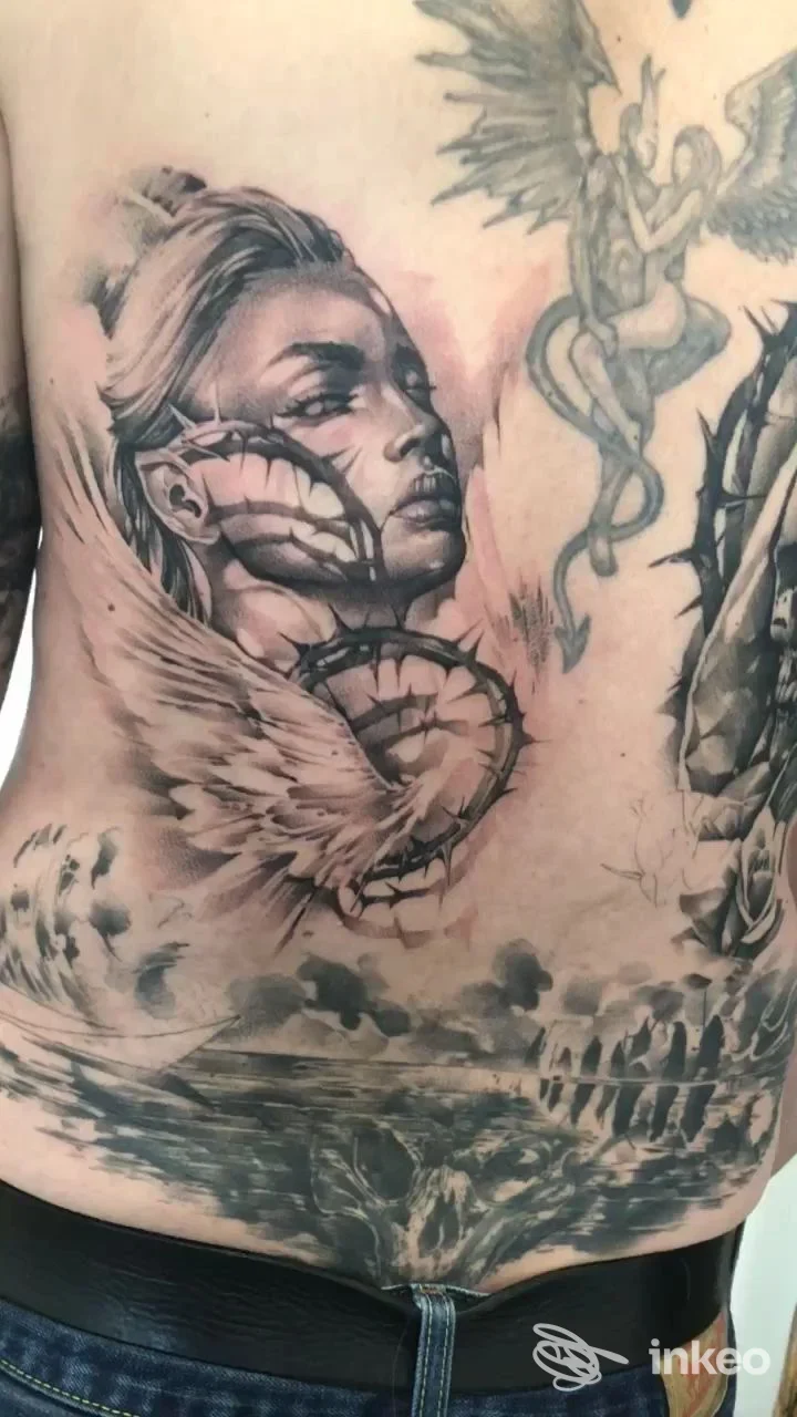 Grande tatuaggio in bianco e nero sulla bassa schiena raffigurante un volto femminile stilizzato con ali e motivi decorativi. Materia Tattoo Lab, Creazzo.