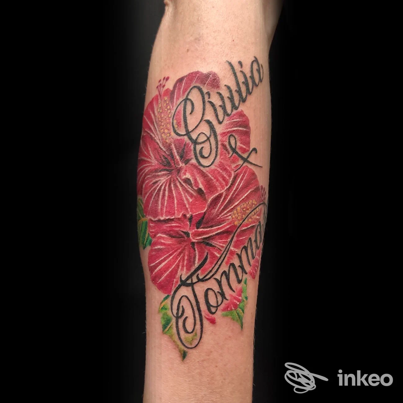 Tatuaggio su avambraccio con grandi ibischi rossi e scritta in corsivo; scatto professionale di Ogm Tattoo Studio Di Micheletto Lara, Valbrenta.