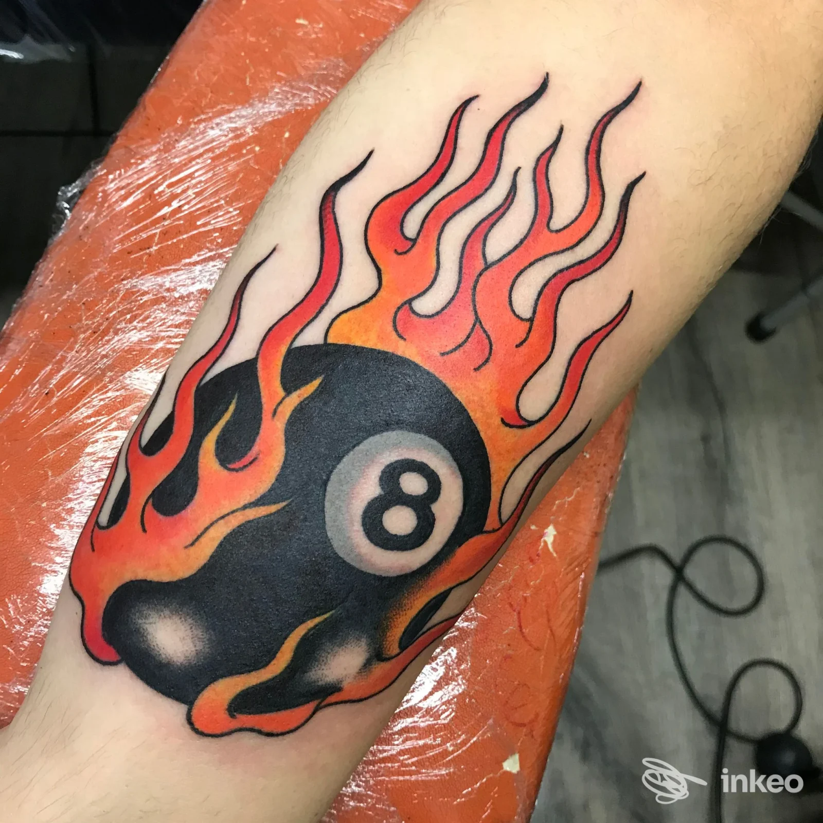 Tatuaggio colorato su avambraccio: palla da biliardo nera con numero 8 avvolta da fiamme rosse/arancioni. RED REAPER TATTOO, Fontane.